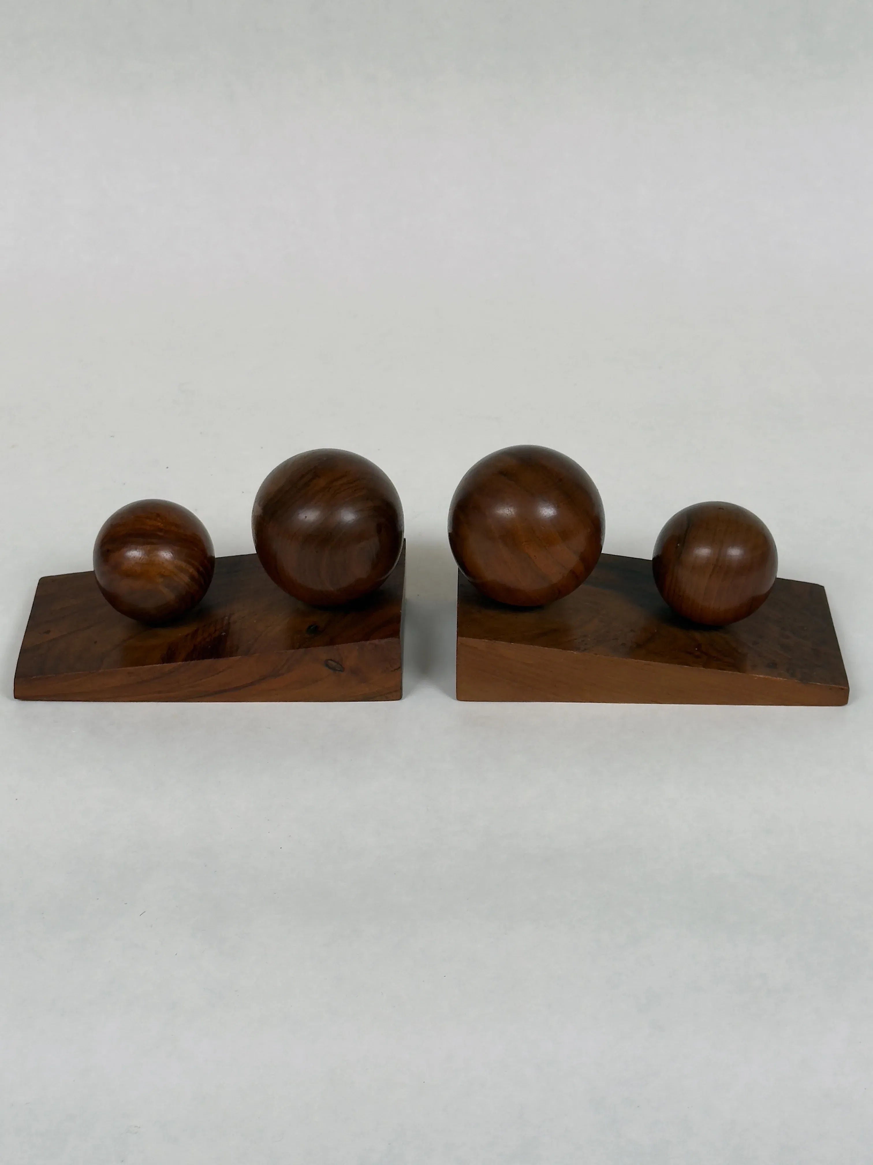 The Art Deco Bookends in Walnut by Galerie Storm are crafted from solid walnut, featuring geometric spherical shapes on rectangular bases that highlight the natural wood grain. Their design suggests balance and symmetry, showcasing smooth surfaces and varying sizes.