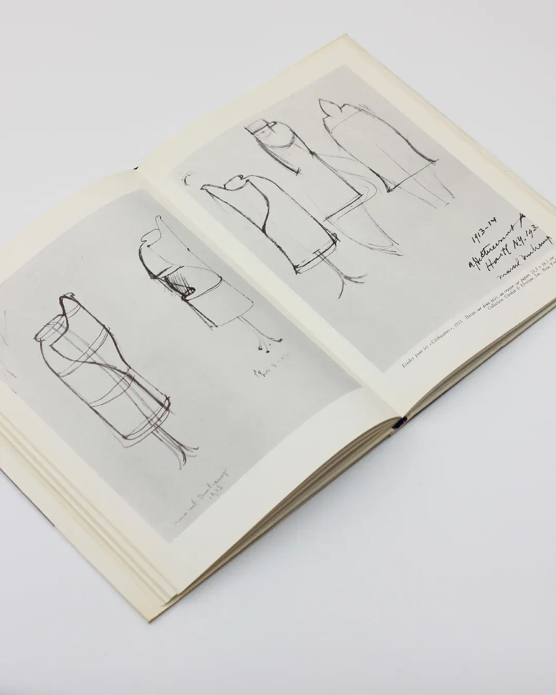 The "Marcel Duchamp by Sarane Alexandrian Book" from Boga Avante Shop presents an open book that resembles an ode to conceptual art. On the left, multiple dress outlines are showcased, while the right page offers detailed sketches accompanied by handwritten notes, all capturing Marcel Duchamp's avant-garde spirit against a simple light background.