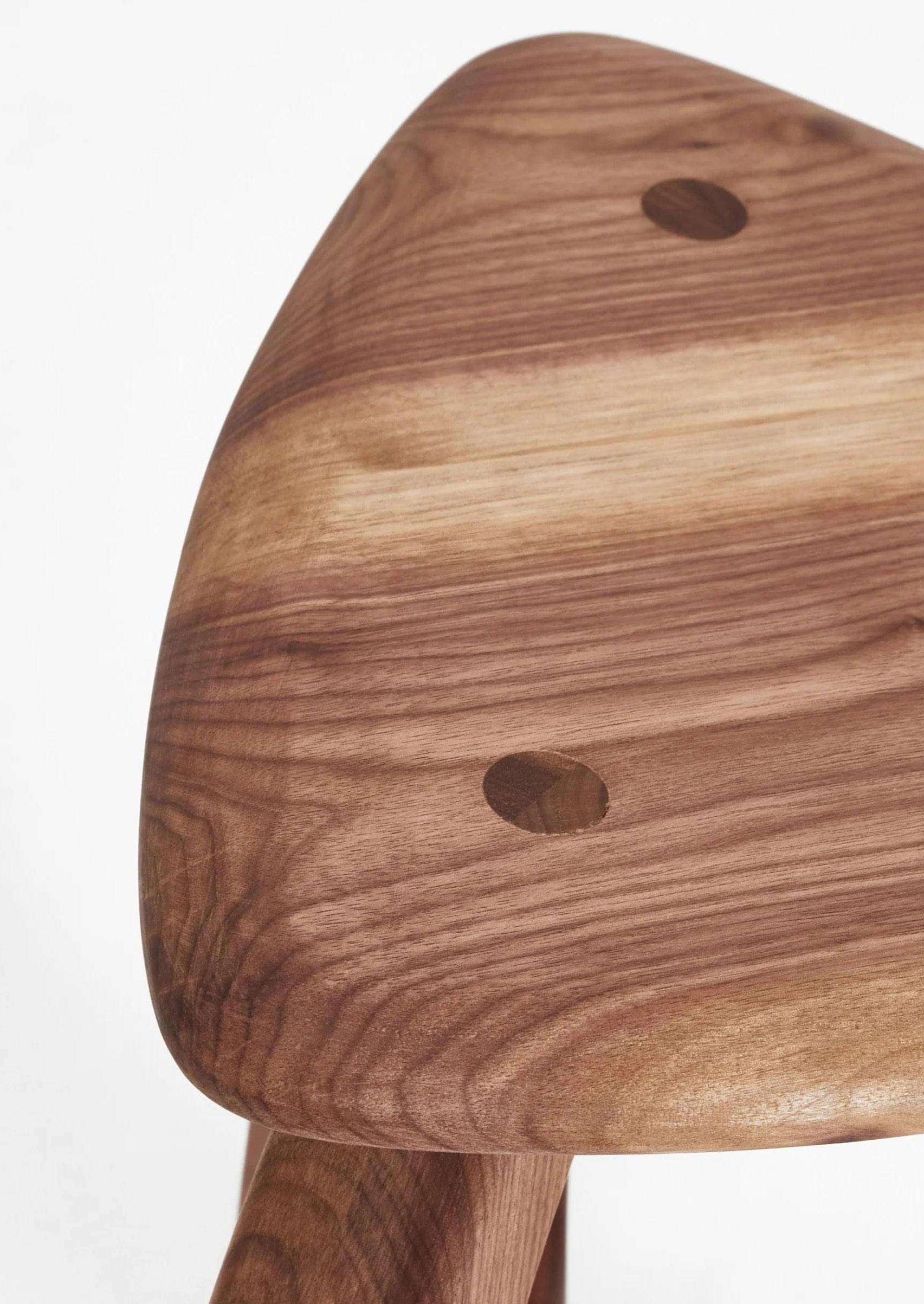 Close-up of an elegant Arc de Stool '52 by Project 213A with a smooth, curved seat featuring visible wood grain patterns and two circular cut-outs. The backrest is not visible, and the focus is on the craftsmanship and texture.