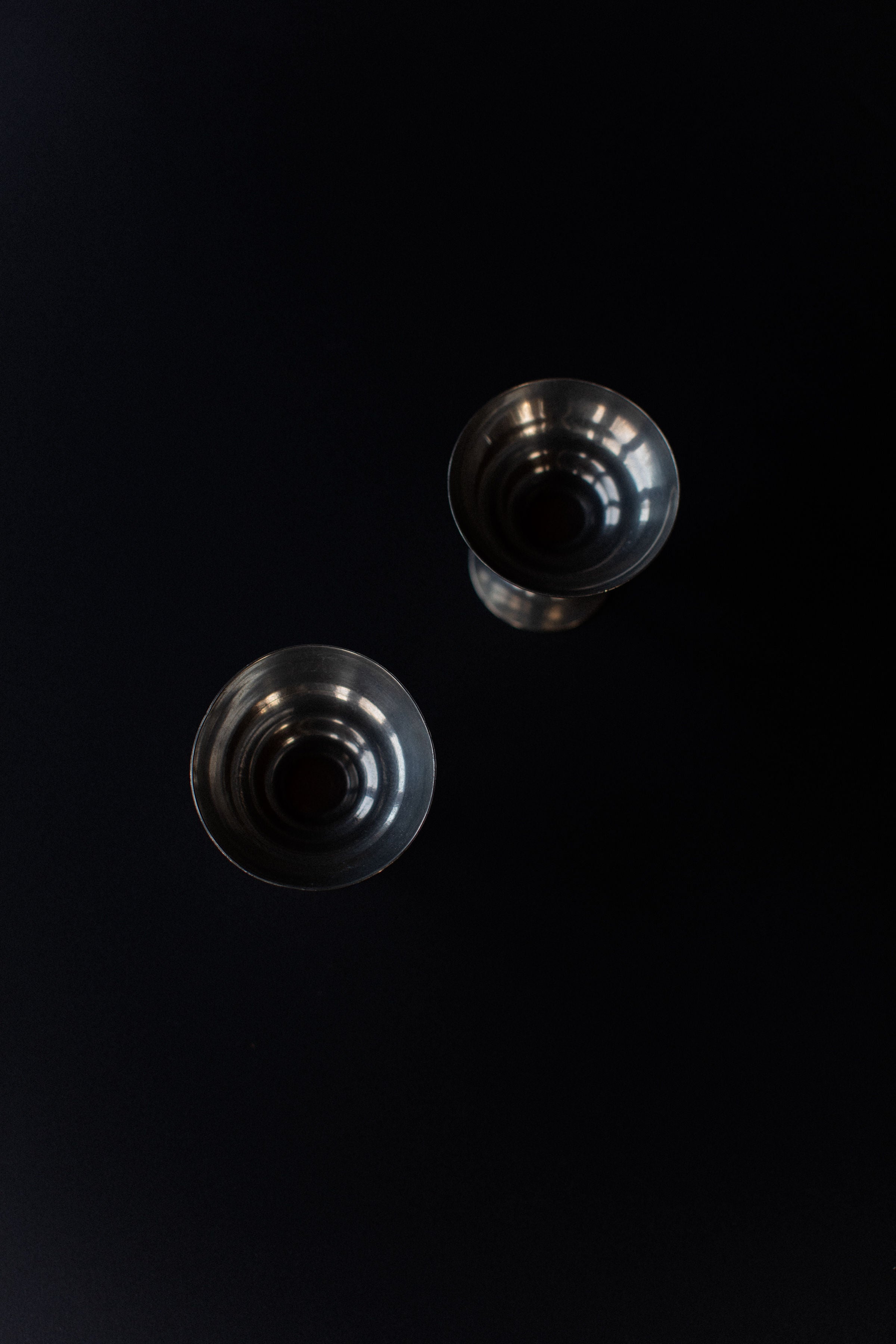 From above, two metallic Out For Lunch Ice Cream Cups rest diagonally on a black surface. Their Art Deco design and vintage style are highlighted by light reflecting off their rims and interiors.