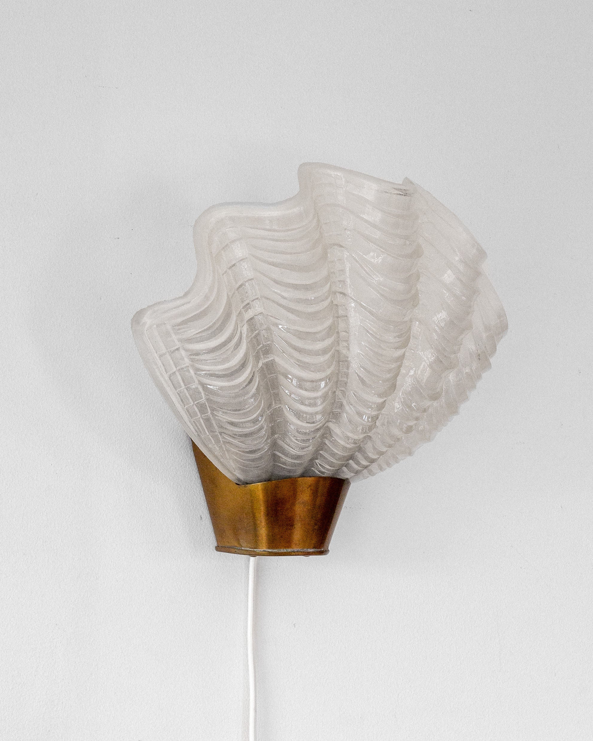 A Spigel Vintage "Coquille" Wall Light from the 1940s in Sweden features a white scallop-shaped glass with a textured pattern, mounted on a bronze base, and includes an elegantly hanging white electrical cord.