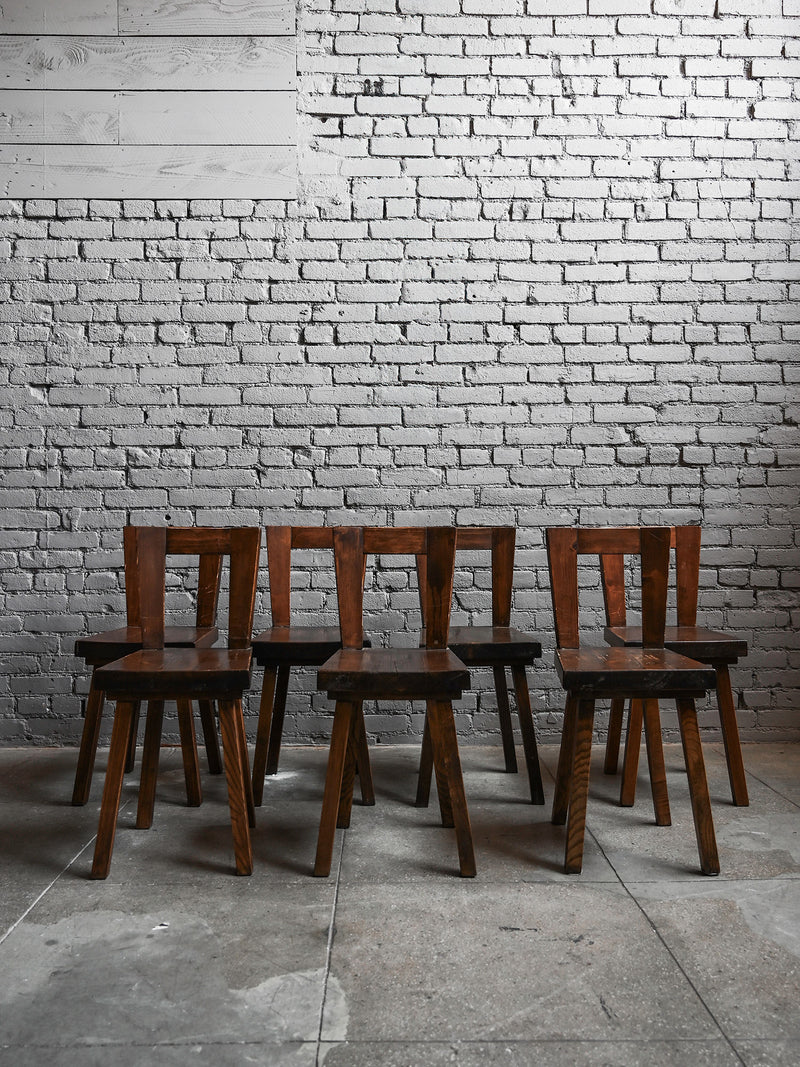 Eight geometric wooden chairs from Studio OSKLO are arranged in two rows against a white brick wall on a concrete floor, showcasing their vintage 40s design in an industrial-style room.