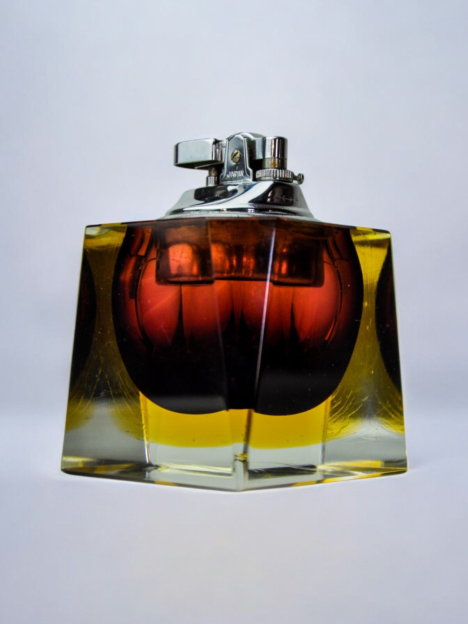 A square-shaped Sommerso Lighter by Seguso from the 70s, crafted in Murano glass, features a metallic top and a transparent base with amber and yellow hues. Presented by Malamar Studio against a plain white background.