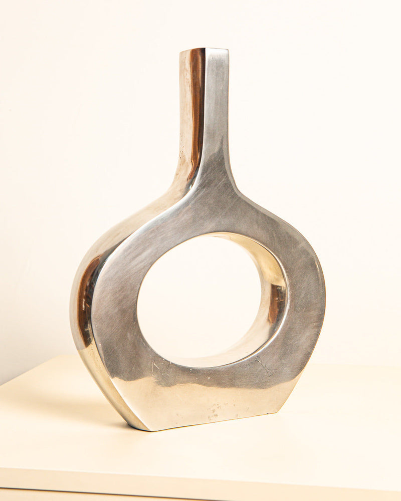 The Treaptyque Large Italian Cast Aluminum Vase 80s features a modern, abstract design with a hollow circular center and narrow upright top, shown on a light surface with a plain background.