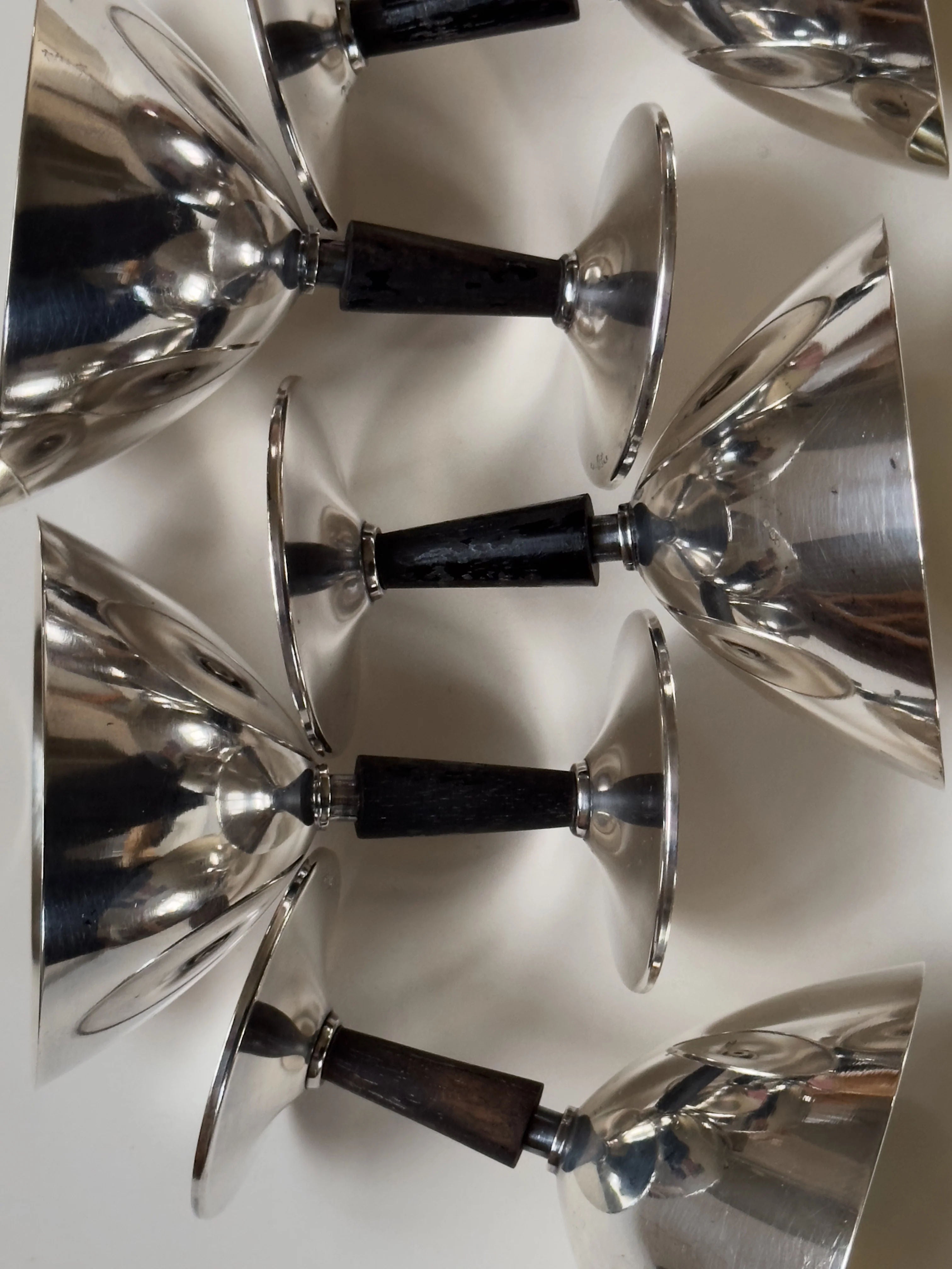 GAB Cocktail Glasses by Galerie Storm feature silver bowls with dark wooden stems, arranged at angles against a light background. They evoke vintage Swedish elegance and create a reflective pattern reminiscent of 1930s cocktail glamour.