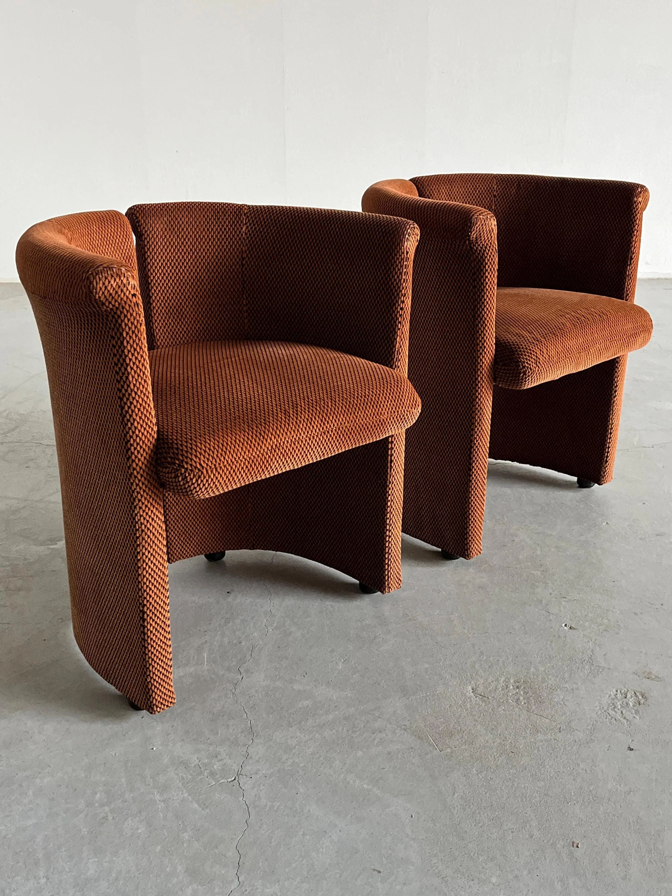 Two Cherry Cargo "Pair of Postmodern Armchairs," barrel-shaped with checkered fabric upholstery, sit on a concrete floor. Their rounded backs and lack of armrests offer a cozy, minimalist look that beautifully combines Postmodern elements with timeless charm.