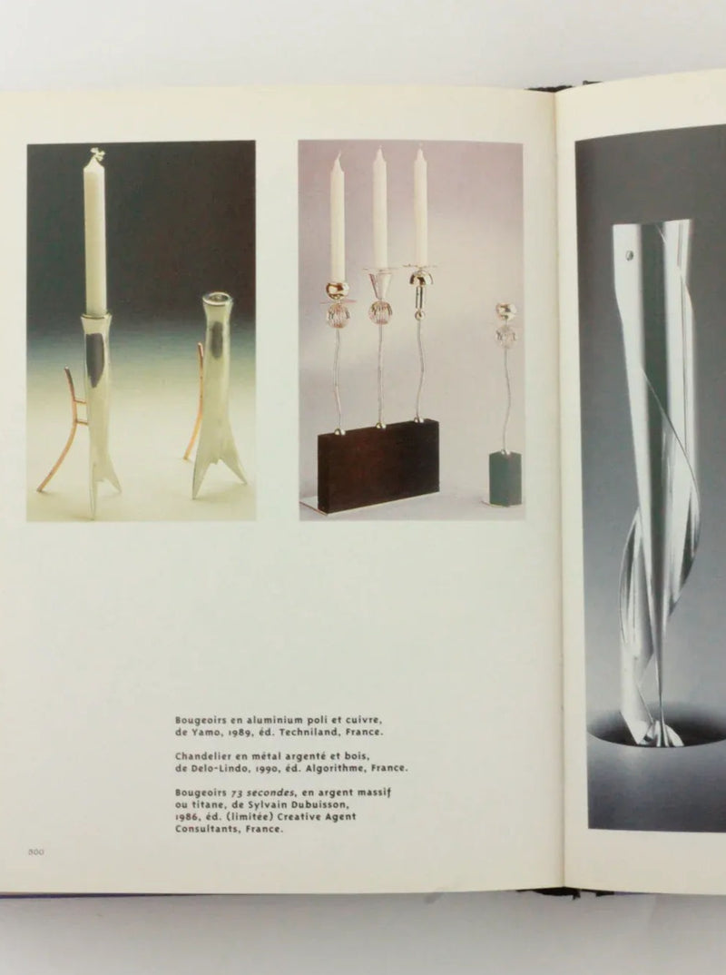 An open Objets Affectifs: Le Nouveau Design de la Table from Boga Avante Shop displays photos of various modern candleholders. On the left page, there are three candleholders: two minimalistic designs and one more intricate. The right page showcases a sleek, twisted metal candleholder with distintivo diseño italiano. Text descriptions are below each image.