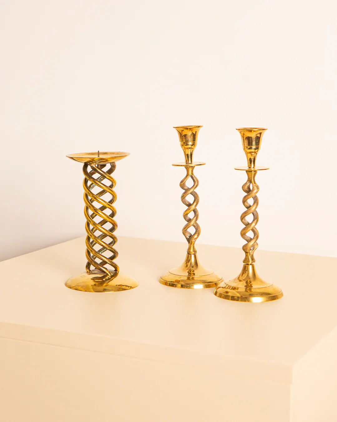 A set of 3 ornate Treaptyque Italian 60's gilded metal candleholders are arranged on a light surface against a plain background, with the tallest holder on the left and the two shorter ones on the right.