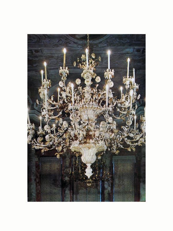 A grand, ornate chandelier with multiple candle-like lights and intricate decorative elements hangs from a ceiling. The Age of Rococo by Maison Plage, reminiscent of 18th century Europe and Rococo art and design, features detailed floral designs and appears to be in a luxurious interior space with a dark, elegant backdrop.