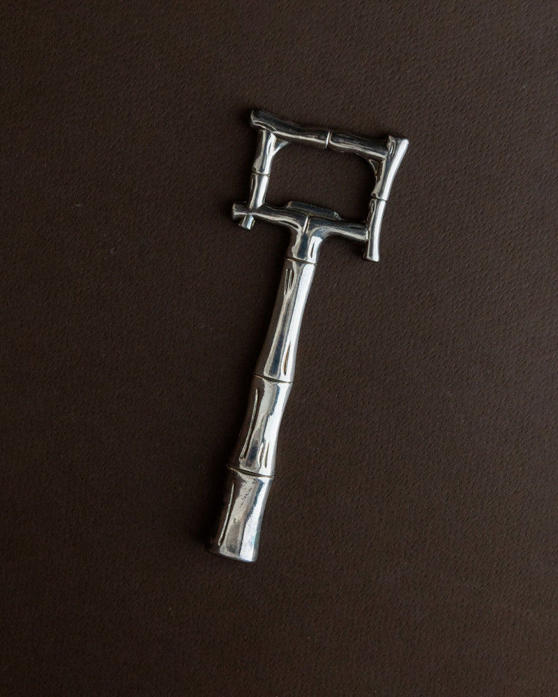 The 1970s silver-plated bottle opener by Bottega Jacobs, designed in a vintage bamboo style, sits elegantly on the dark brown surface.