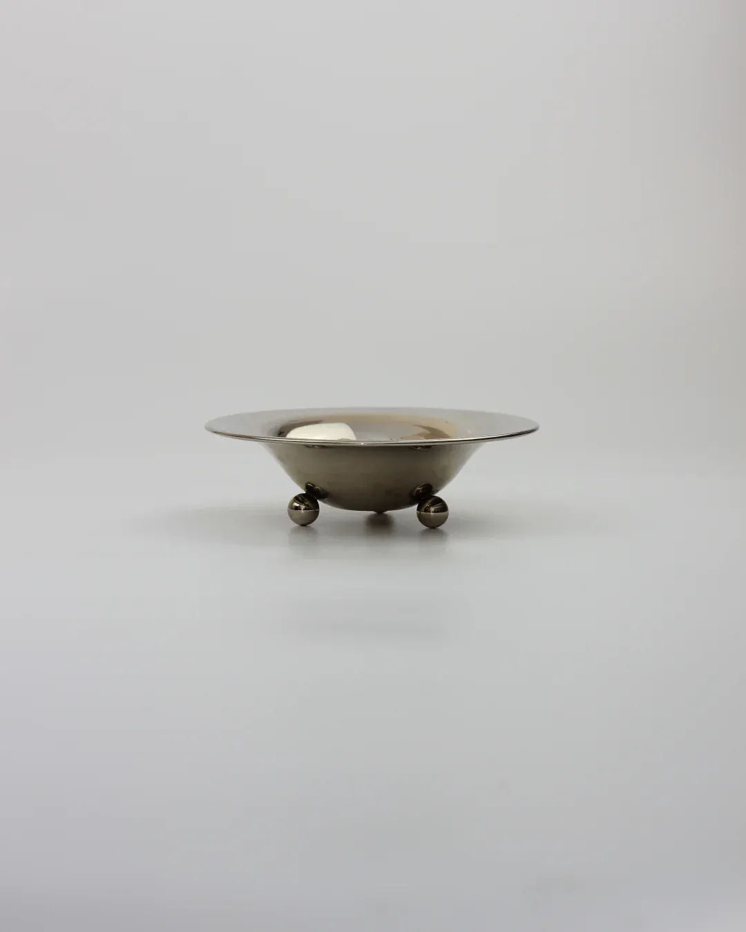 The Boga Avante Shop's Bowl on Three Legs is a metallic alpaca design with a shallow structure and wide, flat rim, ideal for serving oysters. It stands on three spherical feet against a plain, light gray background.