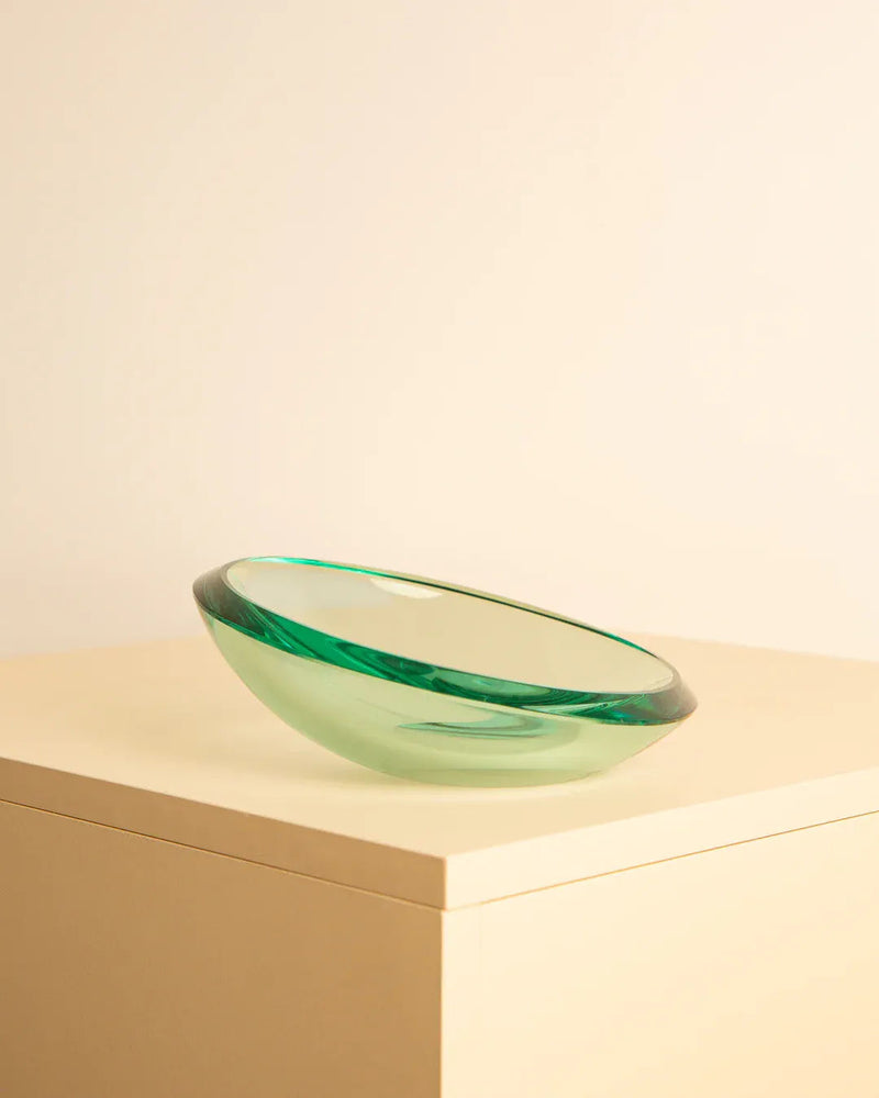 A shallow, green, glass bowl with a translucent appearance sits on top of a beige surface against a light-colored background. Reminiscent of Treaptyque's timeless elegance, the Large circular vide-poches by Fontana Arte 60's has a gently curved shape and smooth rim, reflecting light softly with every angle.