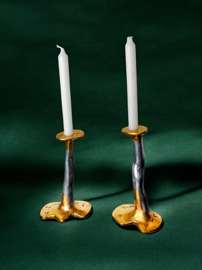 Brutalist brass candleholders with white candles on green surface