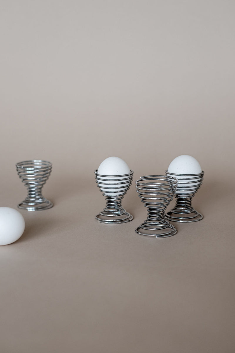 Wire spiral egg cups holding white eggs on wooden surface