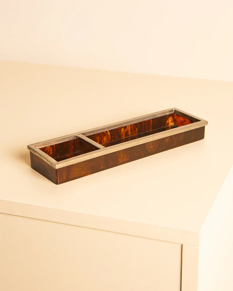 The Vide Poches Italian 80s by Treaptyque is a rectangular brown tray with a silver edge, showcasing Italian design on a light beige surface. It features a glossy finish and tortoiseshell effect, elegantly divided into two sections.
