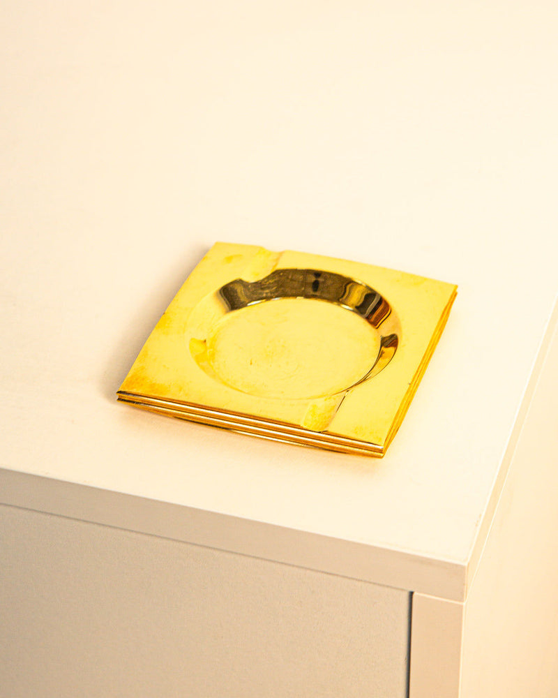 The Brass Ashtray by Francois Gross 60's from Treaptyque sits on a white table, its shiny brass surface reflecting light in classic 60s style.