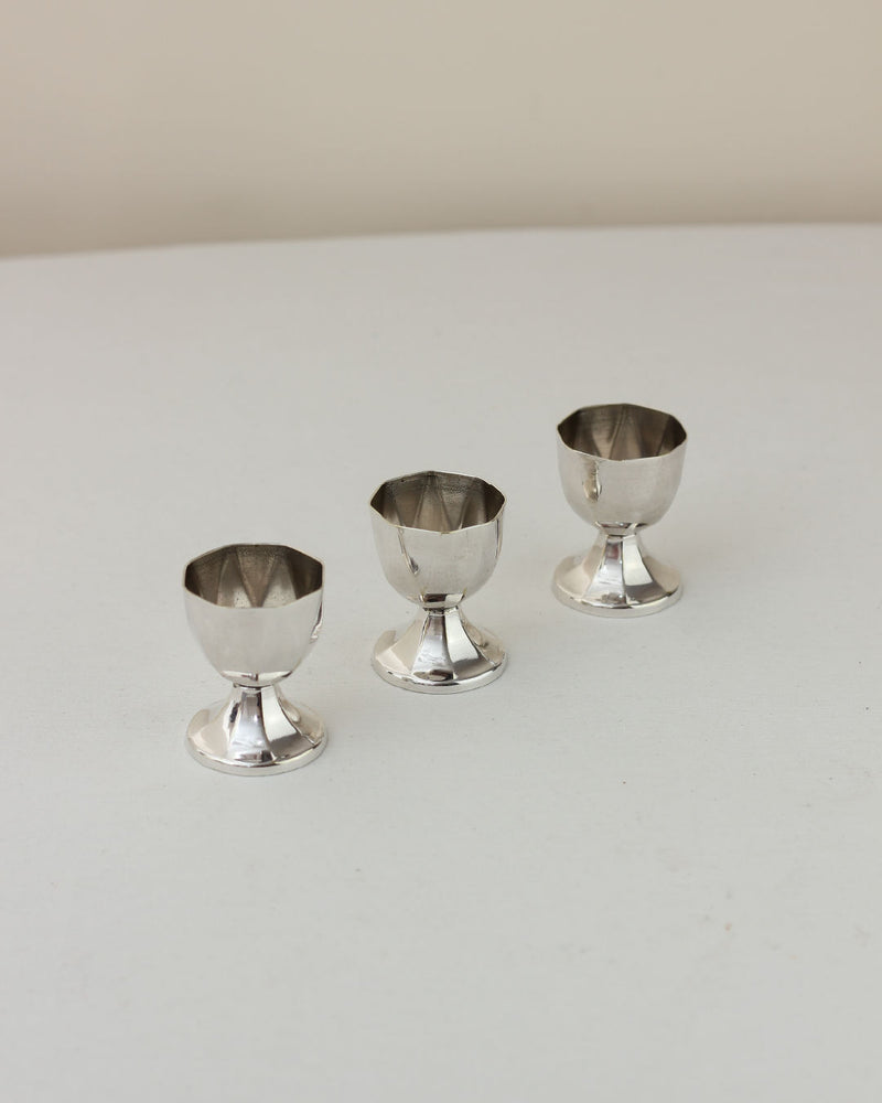 Three vintage silver egg cups arranged in ascending size on white surface