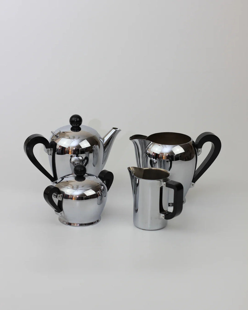 A set of four shiny metal Boga Avante Shop Italian Coffee and Tea Set, 1945 teapots and pitchers with black handles and lids, arranged on a plain white background, reflecting mid-20th century craftsmanship.