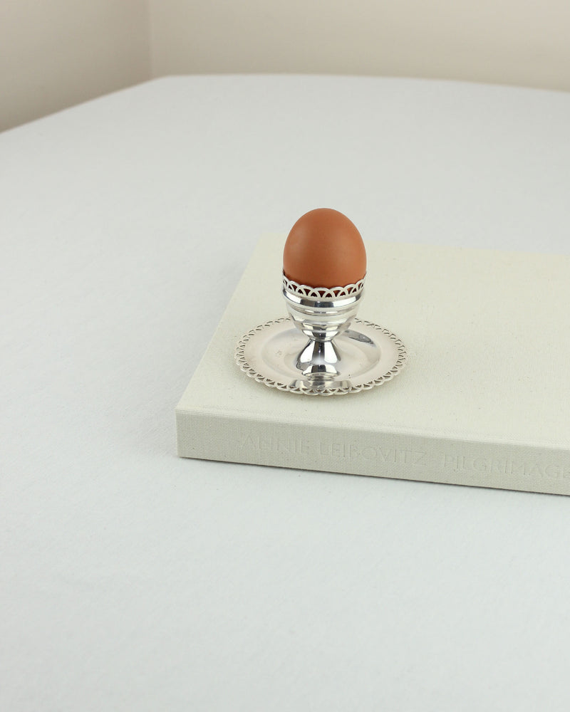 Silver egg cup with decorative rim on matching plate, styled on white surface