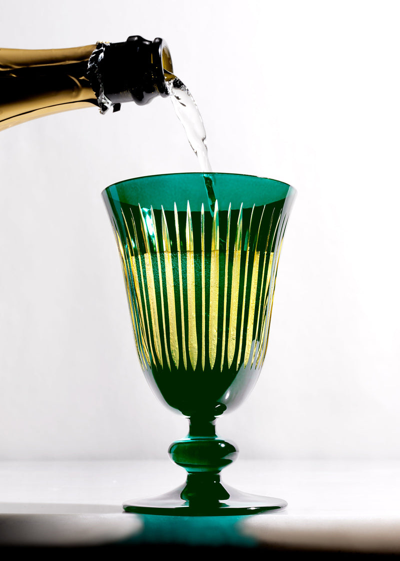 Green crystal wine glass with vertical cut pattern being filled with champagne