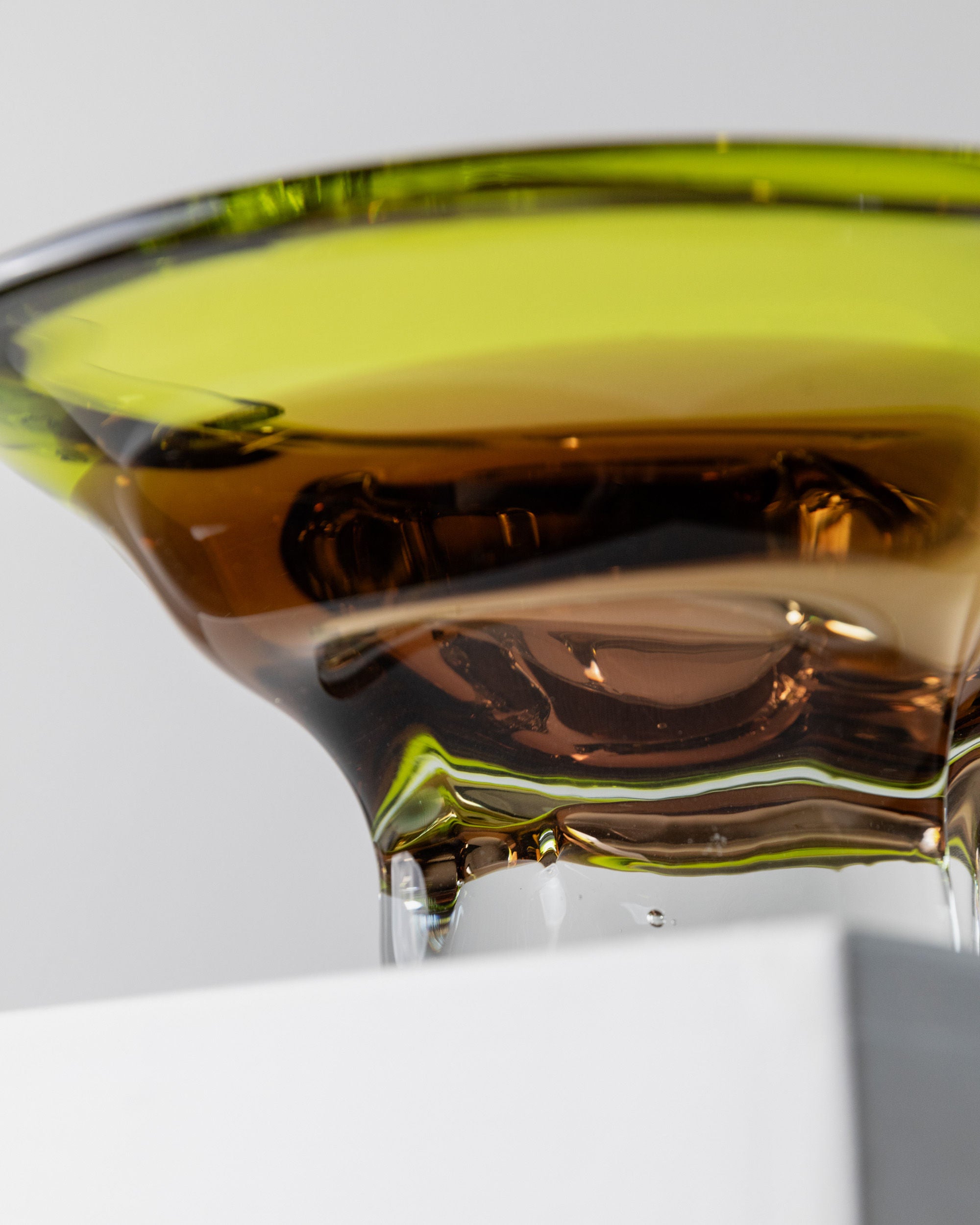 Close-up of a Bottega Jacobs Murano Glass Bowl, Italy 1970s, featuring a shallow, circular dish in translucent green and brown. The smooth, reflective surface displays elegant curves and dynamic colors against a light background, showcasing exquisite Italian craftsmanship.