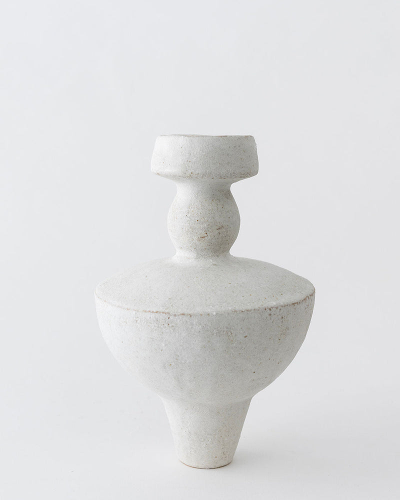 The Lydion Blanco Hueso ceramic vase by Canoa Lab features Mediterranean-inspired texture, a rounded base, wide flat middle, and narrow sculpted neck, beautifully set against a plain white background.