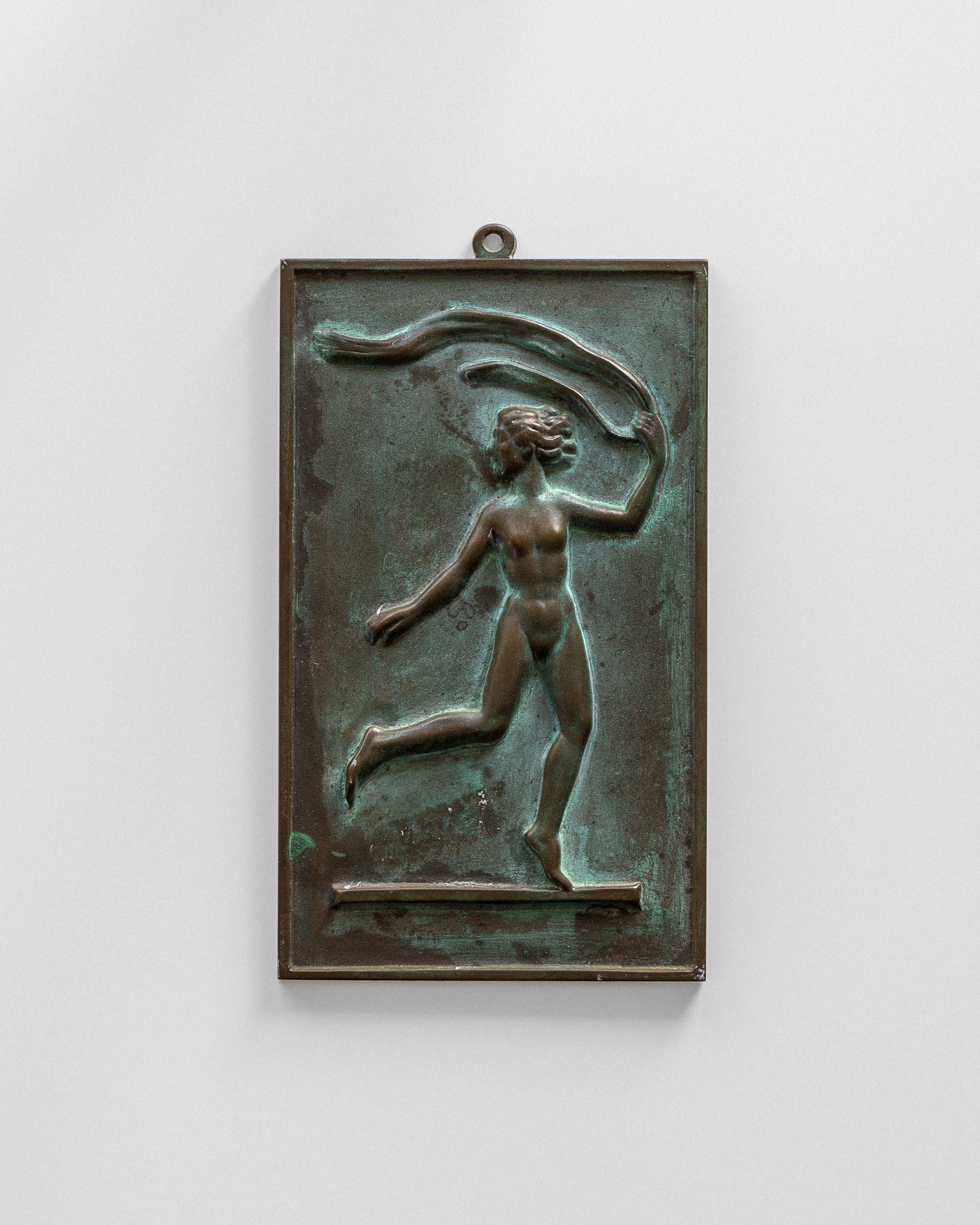 The Bronze Wall Relief by David Jahrl from Spigel features a nude figure in motion with flowing hair and a ribbon, reminiscent of Swedish Grace style. It captures dynamic grace against a rectangular backdrop and includes a hanging loop.