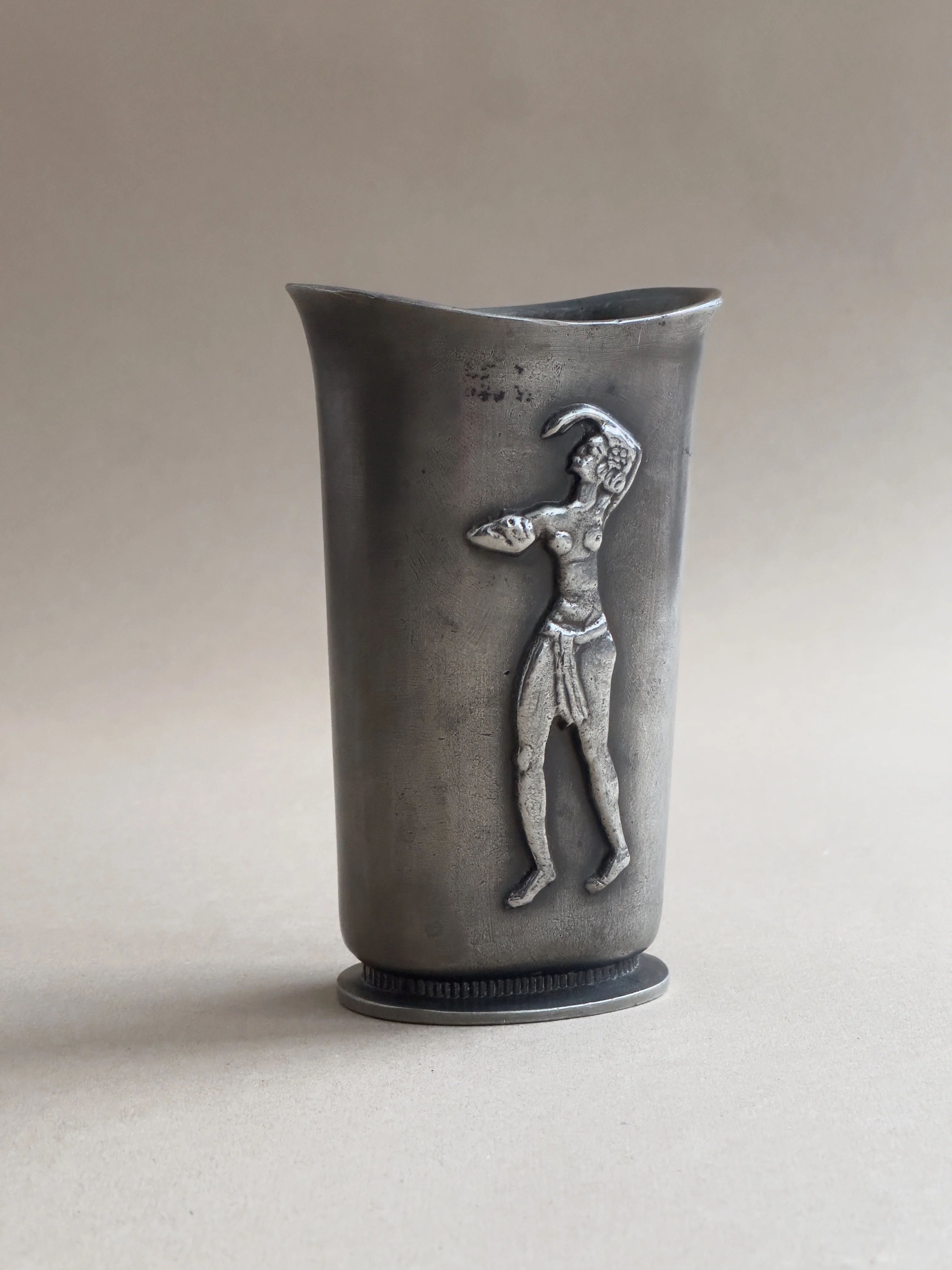 A GAB Art Deco vase from Galerie Storm, crafted in cast pewter, features a tall dark design with a raised relief of a classical male figure in motion. Its detailed musculature reflects the elegance of Swedish Grace against a light gray background.