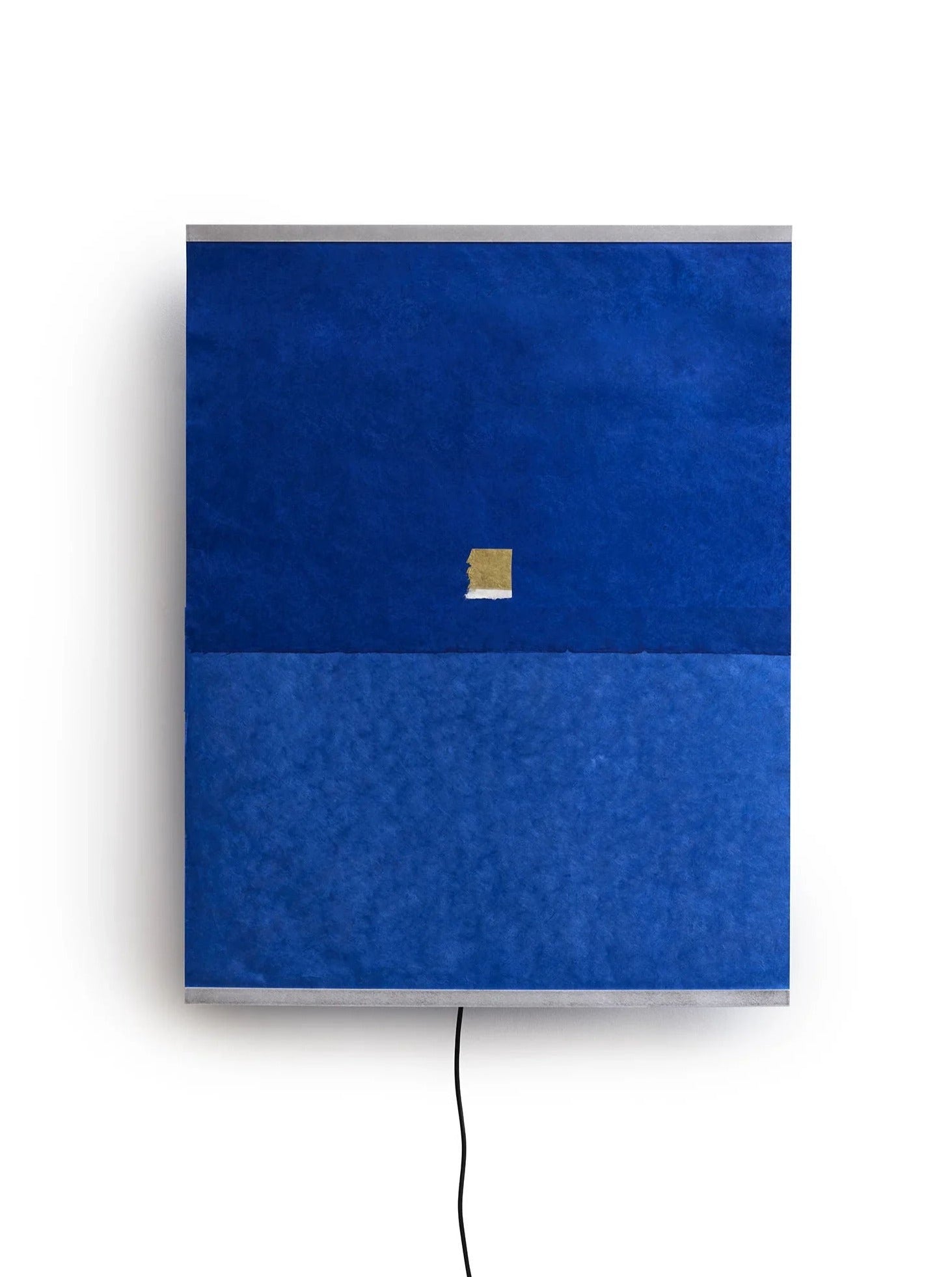 The Panel Wall Lamp – Montenegro by TEGET resembles a square art piece with two blue sections divided horizontally. The top showcases a darker blue color, accentuated by a small gold rectangle at its center. From the bottom, a black cord extends gracefully, embodying the handmade elegance of Ana Kraš.