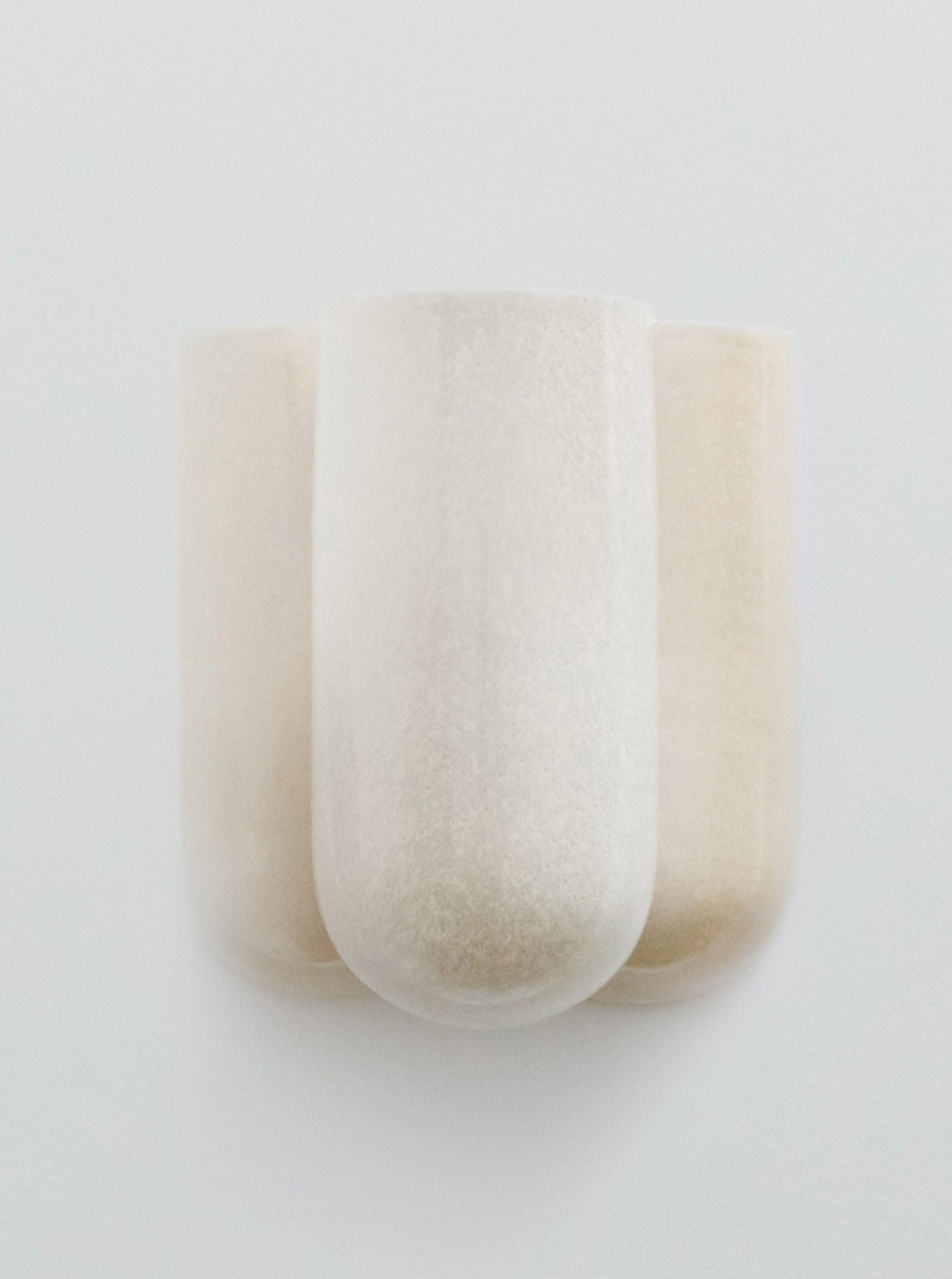 The Wall lamp MOOR PLUS BRILLANCE by Lisa Allegra is a minimalist, white, wall-mounted fixture featuring a smooth, rounded, sculptural design composed of three vertical cylindrical shapes joined together. Its slightly frosted texture and subtle glaze effects impart a soft, modern look.