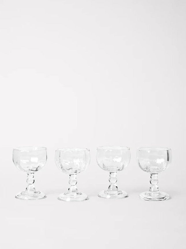 Four empty Alban Wine Glass Small goblets by Akua Objects of varying sizes arranged in a line against a plain, light gray background.