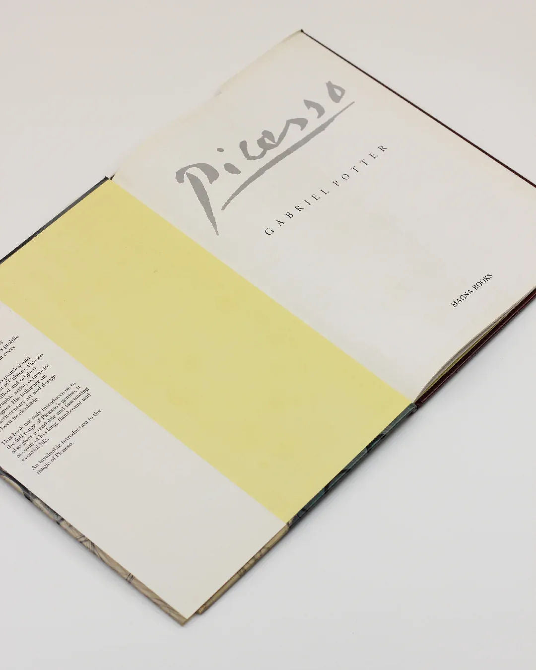 An open book titled "Picasso by Gabriel Potter Vintage Art Book" from Boga Avante Shop lies elegantly on a white surface. The left page is blank and yellow, while the right showcases the title and author's name, paying homage to the iconic Spanish artist's influence on modern art.