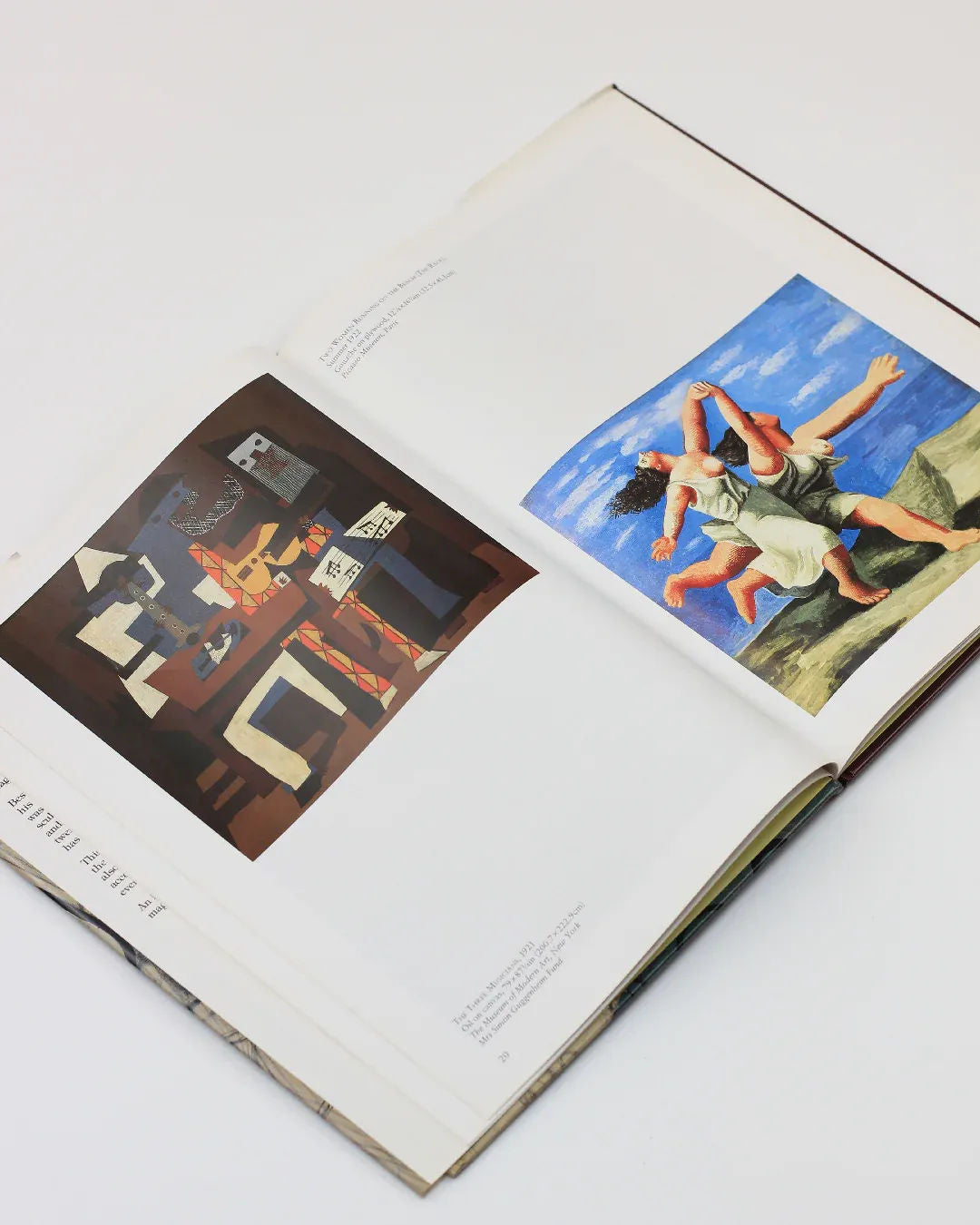 Displayed in the open "Picasso by Gabriel Potter Vintage Art Book" from Boga Avante Shop, one page showcases a cubist-style piece reminiscent of Picasso, featuring abstract shapes in muted tones. The opposite page captures a vividly modern scene of two figures wrestling by the sea against a bright blue sky.