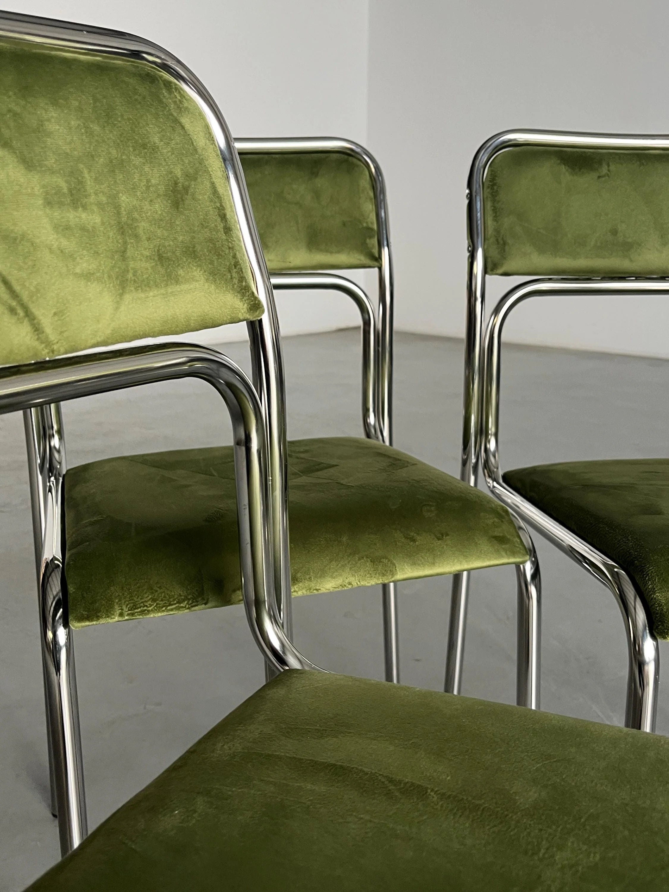 A minimalist room with a light gray floor and white walls features three Cherry Cargo Bauhaus-inspired chairs, showcasing their green velvet textures and tubular chrome frames, embodying an Italian modernist aesthetic.