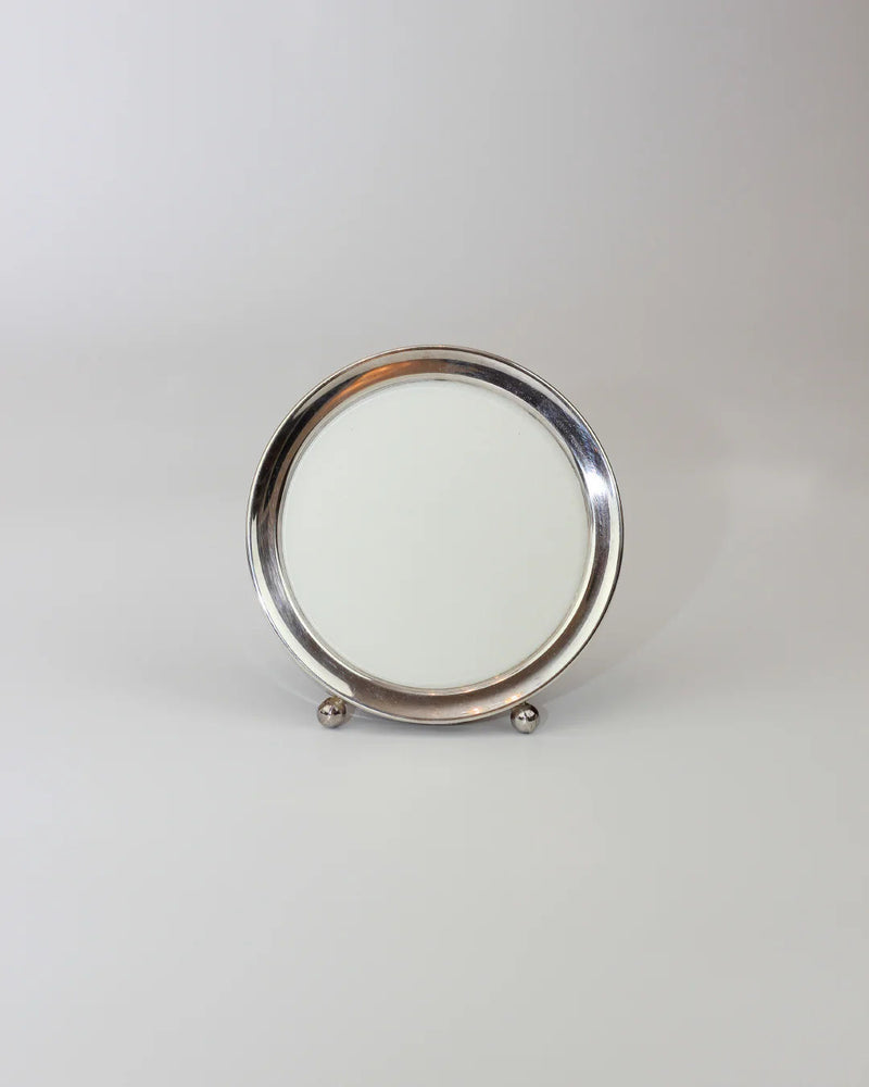 The Round Art Deco Mirror by Boga Avante Shop features a round silver frame and plain white center, standing on two spherical feet against a light gray backdrop.