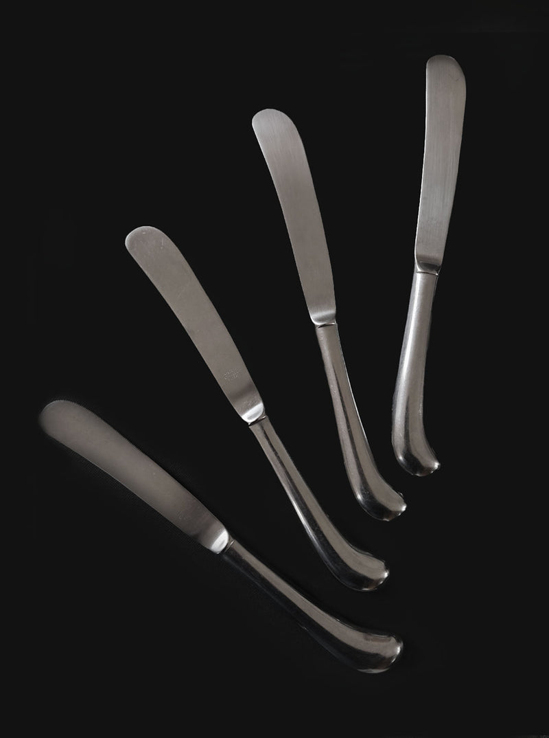 A set of 4 Les Objoies butter knives, crafted from stainless steel with smooth, slightly curved handles, are artistically arranged against a black background, showcasing modern Korean tableware elegance with their rounded ends pointing outward.