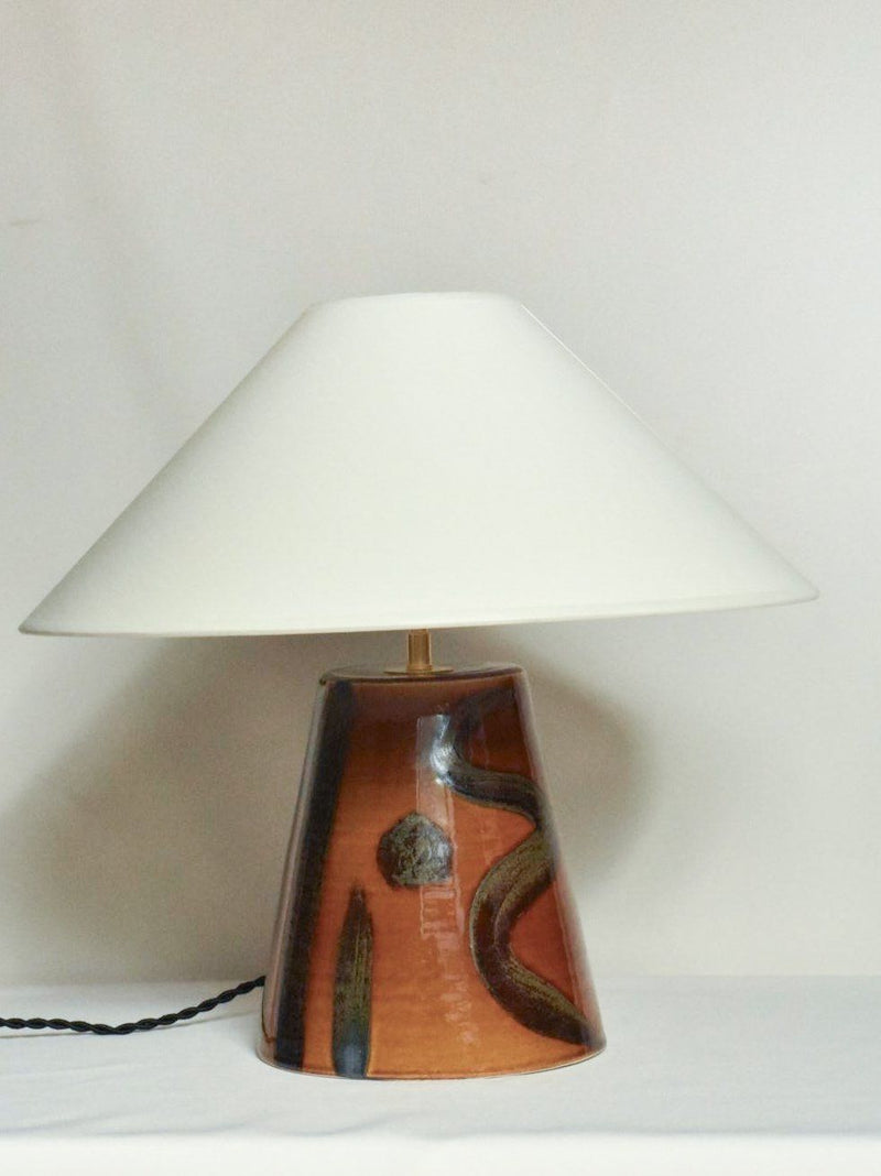 The 'Sierra' Table Lamp by Landy Rakoto Ceramics features a hand-painted brown base with abstract patterns and a wide white conical shade, inspired by the Loire Valley, displayed against a plain white background.