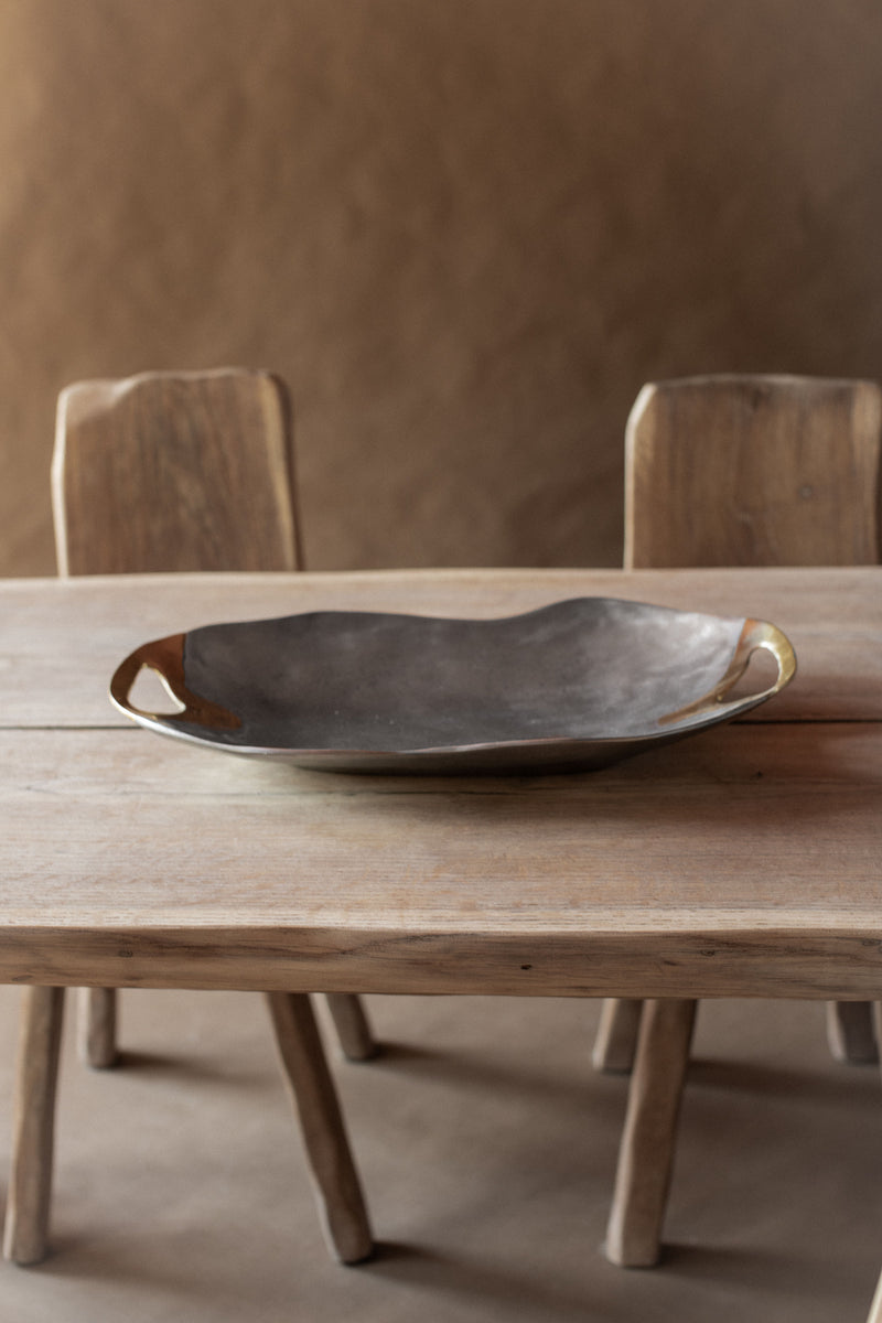 Dark ceramic brutalist bowl with brass handles on wooden dining table