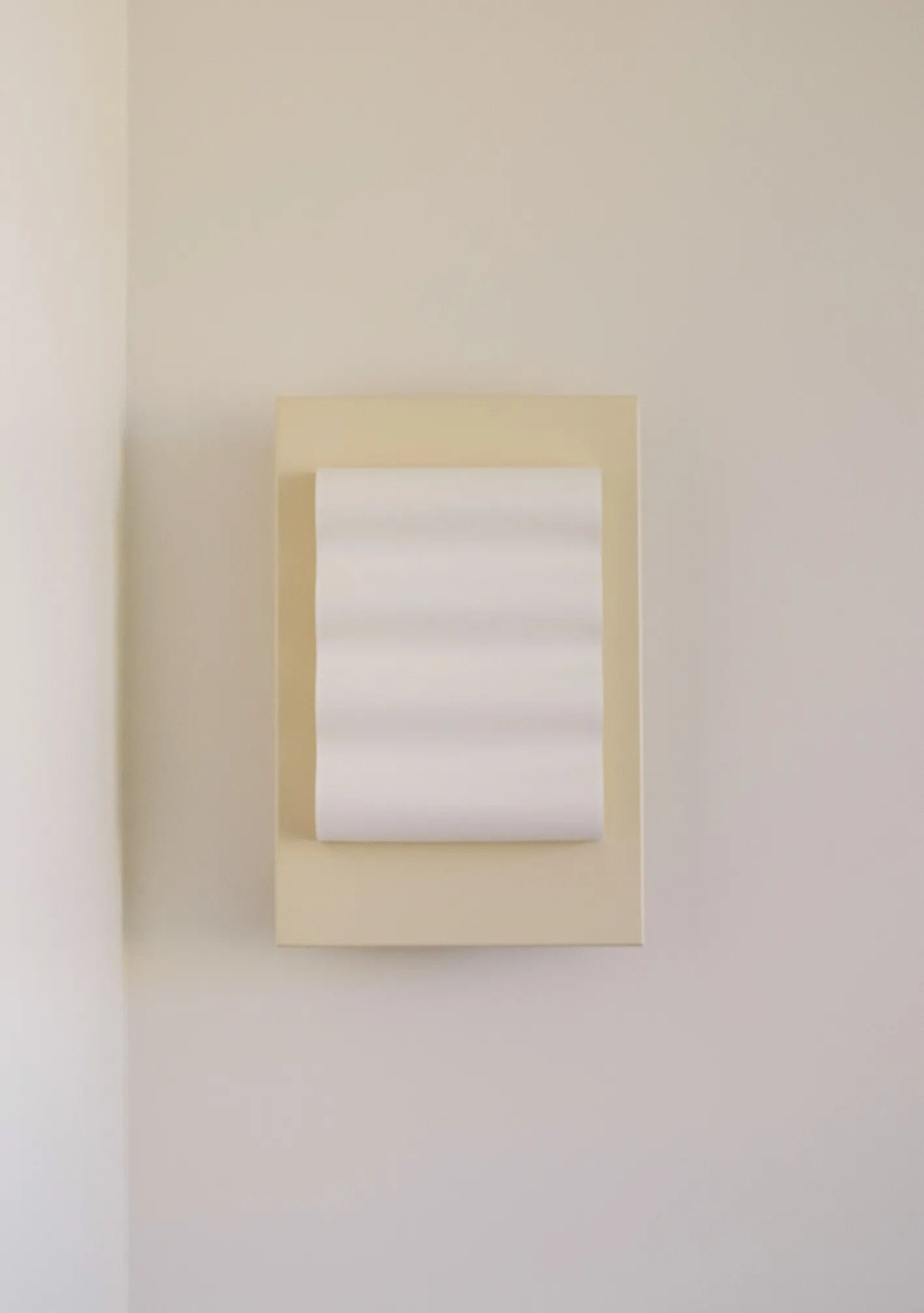 The Wall Light Frame OW S by Violaine d'Harcourt graces a light-colored wall with its minimalist design. Its rectangular frame showcases a wavy, textured surface that elegantly protrudes, casting soft shadows and embodying handcrafted elegance.
