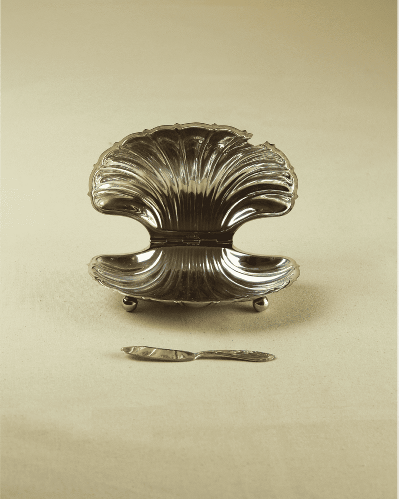 Silver shell-shaped butter dish with ornate ridged design and legs