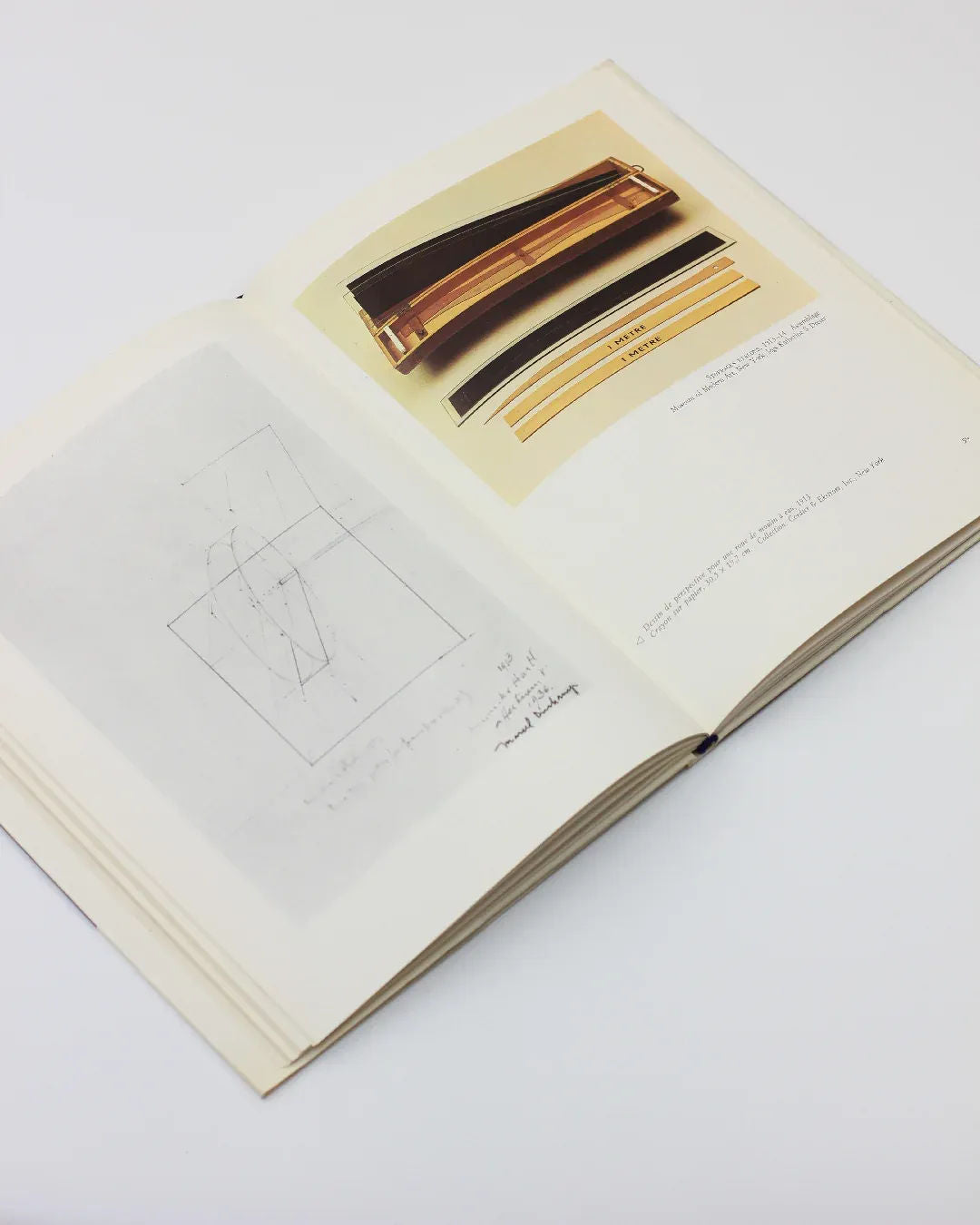 The "Marcel Duchamp by Sarane Alexandrian" book from Boga Avante Shop is open, revealing architectural diagrams and a photograph of a metal structure that echo the thought-provoking style of conceptual art. The pages are adorned with technical drawings and notes, highlighting design and structural details against a simple, light background.