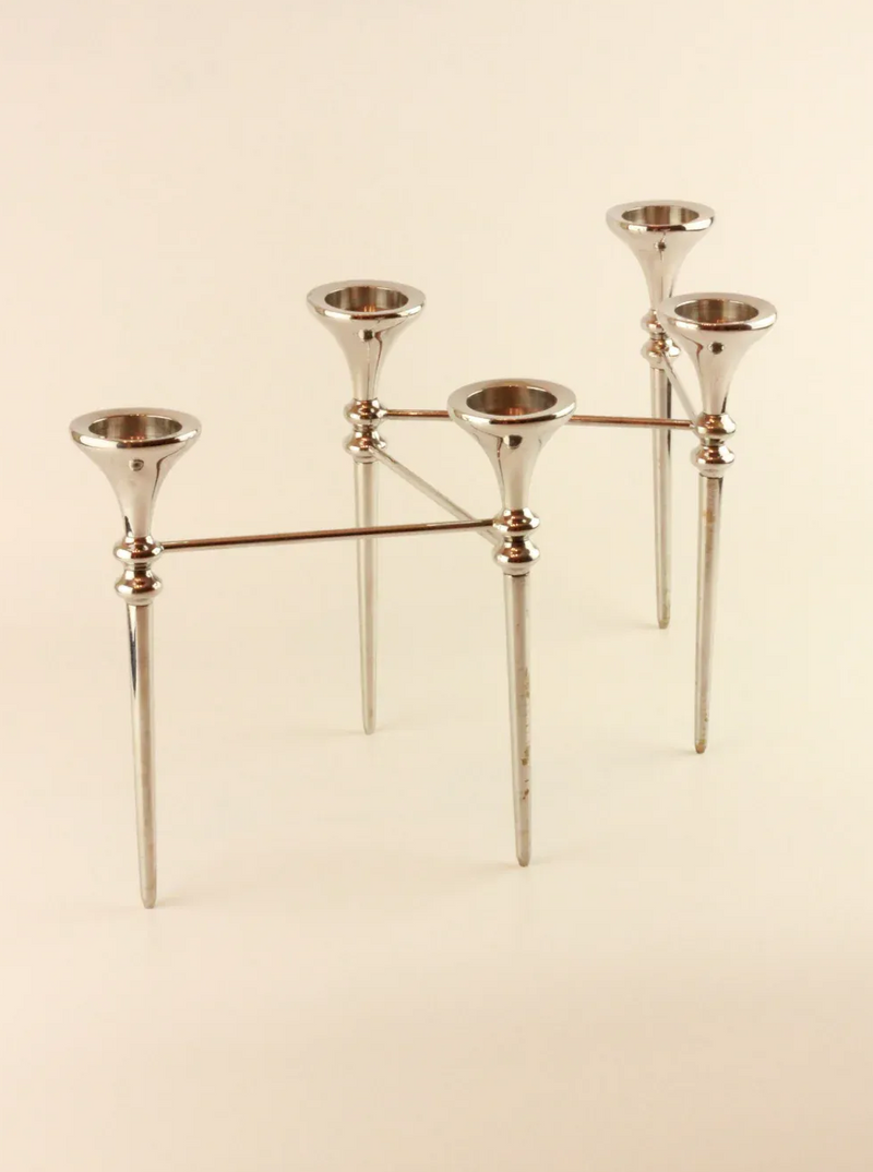 A polished silver Scandinavian Modular Candelabra with a modern, minimalist design featuring five candle holders arranged in a geometric pattern, connected by modular arms from Boga Avante Shop. The candelabra stands on five pointed legs, reminiscent of a 70's chandelier, giving it a balanced and elegant appearance.