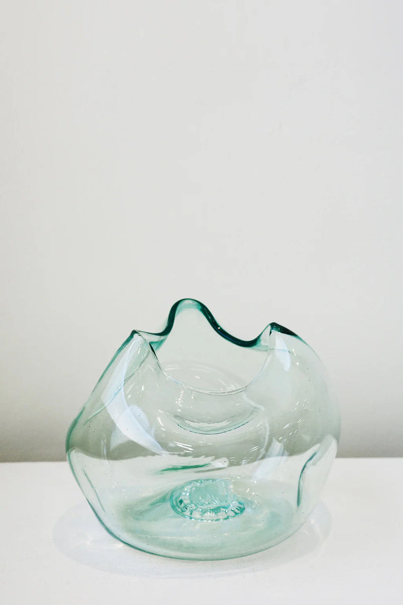 Against a plain white background, 'The Bubble to End all Bubbles' by Completedworks showcases its smooth, abstract design. Made from recycled glass with wavy edges, this clear vase catches the light to highlight its artistic and organic shape.