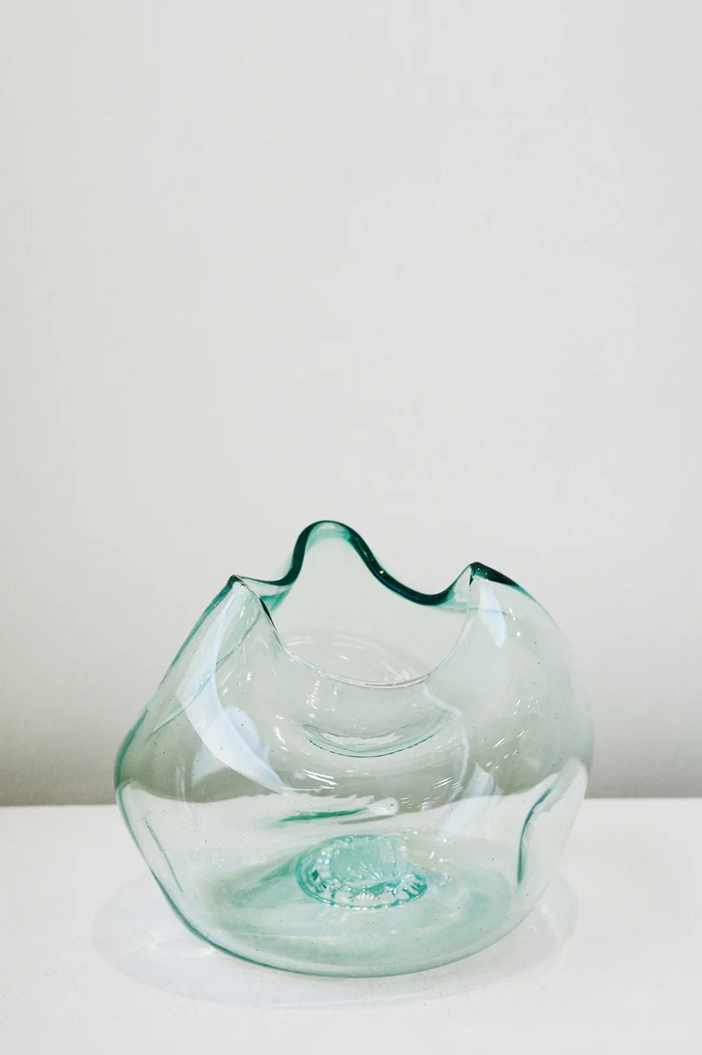 Against a plain white background, 'The Bubble to End all Bubbles' by Completedworks showcases its smooth, abstract design. Made from recycled glass with wavy edges, this clear vase catches the light to highlight its artistic and organic shape.