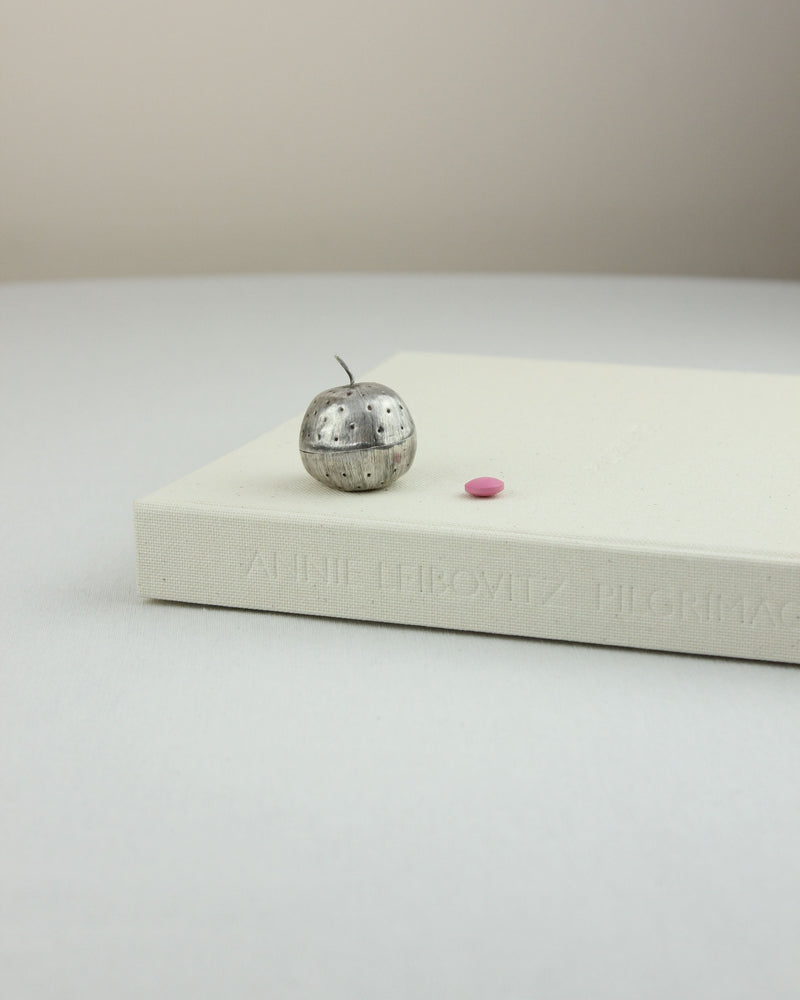 Sterling silver apple pillbox with pink pill on white book