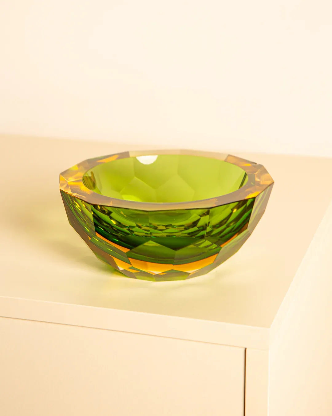 A Large “Diamant” Vide-poches by Flavio Poli from Treaptyque, with a faceted design and translucent green Murano glass, sits on a light beige surface. It captures light to reveal varying shades of green and hints of yellow, creating a prismatic effect reminiscent of Italian design.