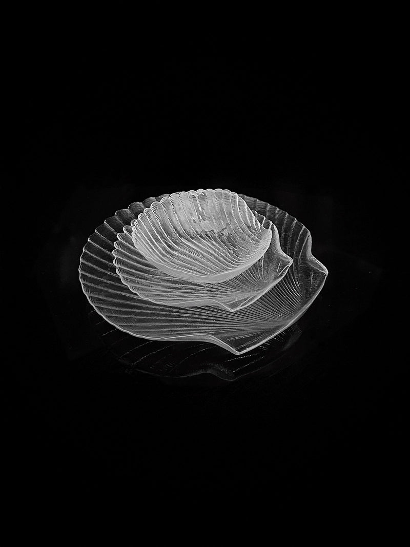 A trio of translucent Glass Serving Dishes by Dodo Vintage, designed in varying sizes with a ribbed seashell pattern, beautifully displayed against a black backdrop—ideal for showcasing culinary delights.