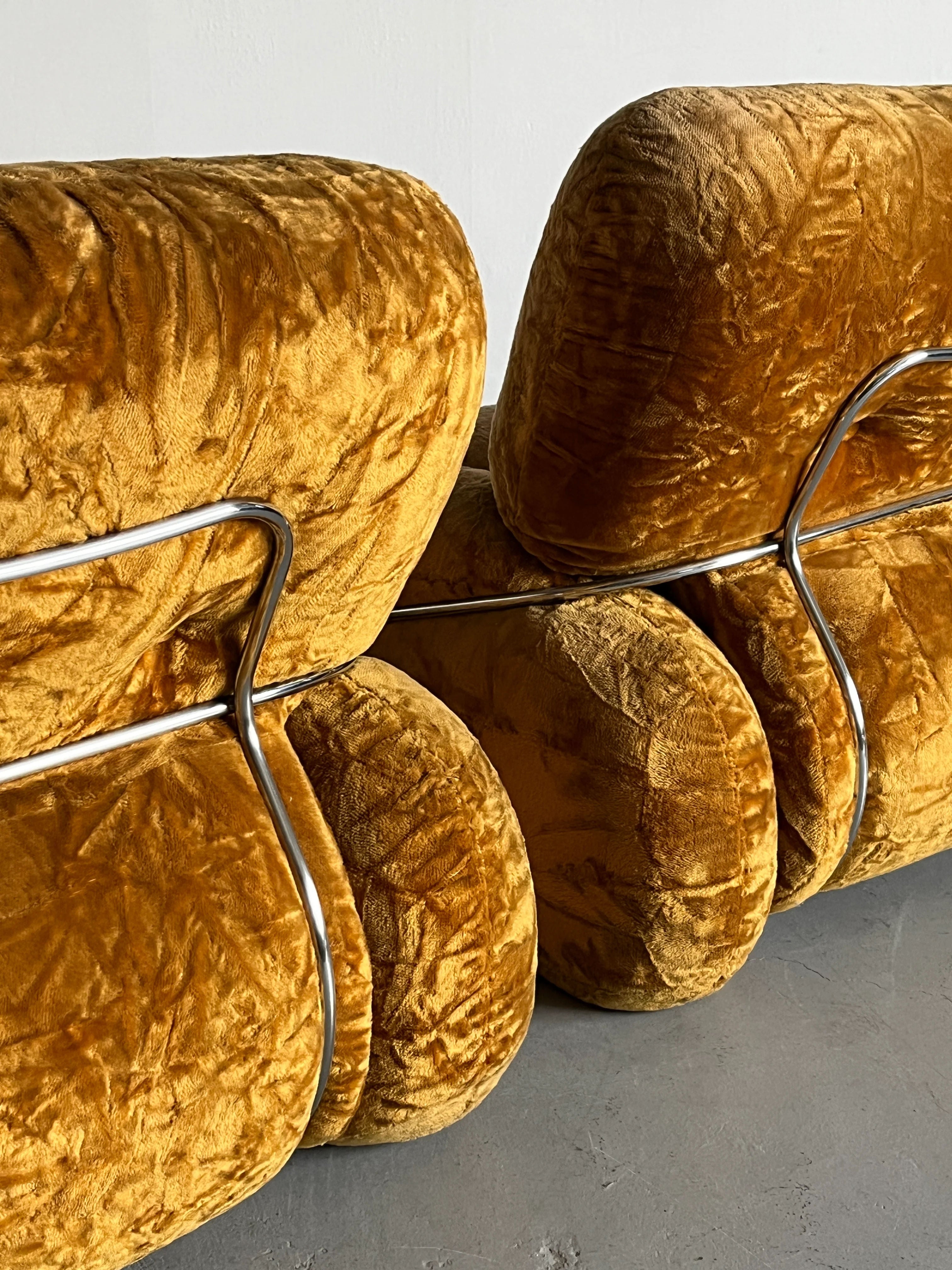 Close-up of two ochre velvet chairs from Cherry Cargo's Adriano Piazzesi 'Okay' Sofa Seating Set. These Mid-Century accents feature modern design with looped metal frames, embodying Piazzesi's style, atop a gray concrete floor.