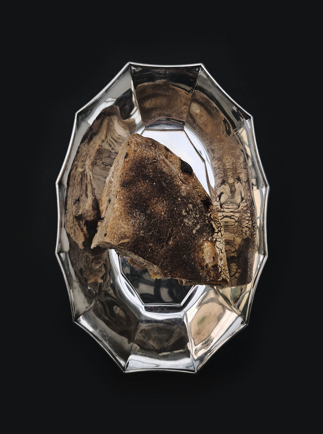 A piece of rustic bread rests on the Les Objoies Silver-plated Tray, featuring a scalloped edge that exudes sophistication against the dark backdrop.