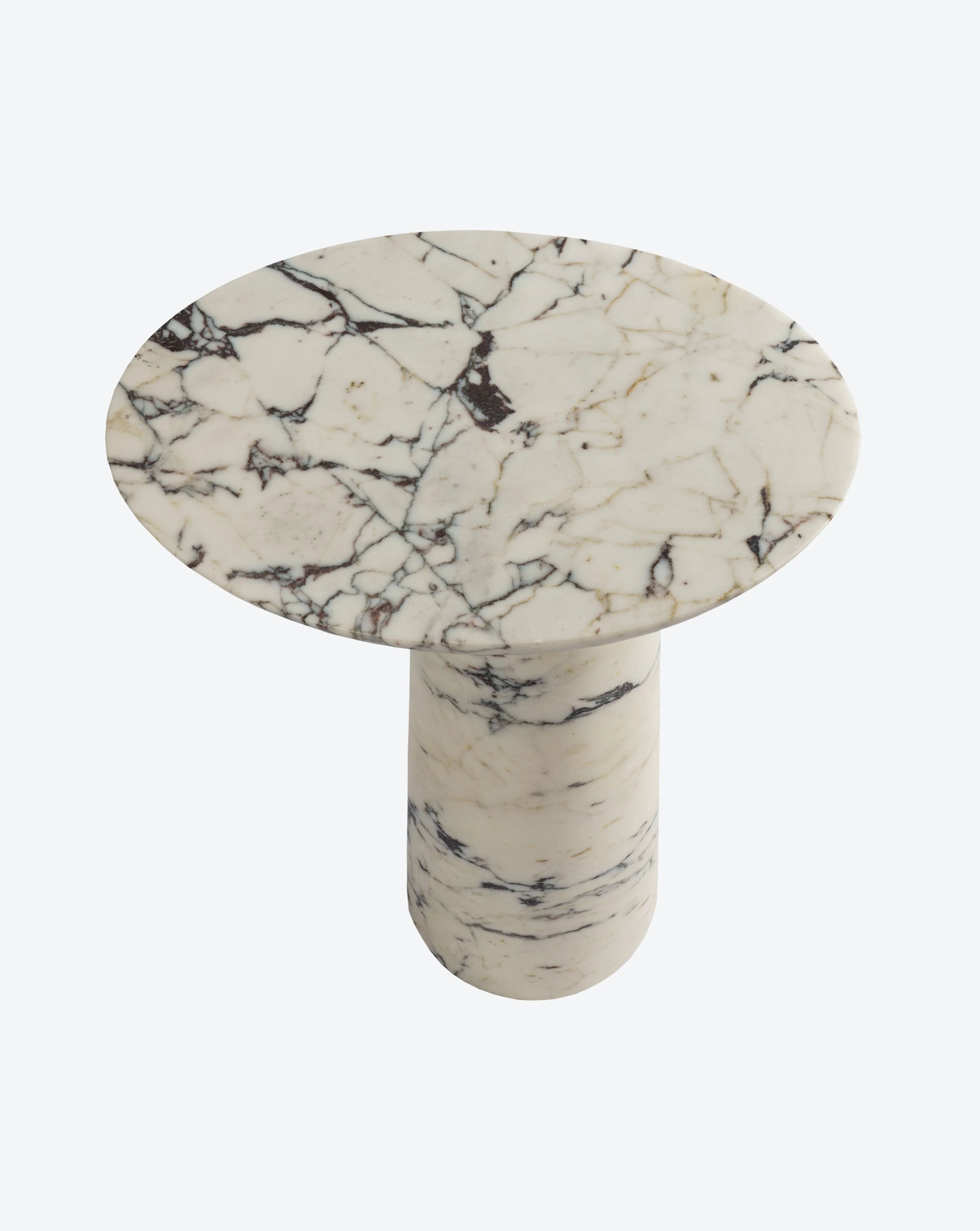 The Athena Marble Side Table by Ransom & Dunn features exquisite Calacatta Viola marble with a round shape and a thick cylindrical base. Its elegant white and black veining is beautifully showcased on a polished surface, enhancing the natural texture of the stone against a light background, emphasizing its European handmade craftsmanship.